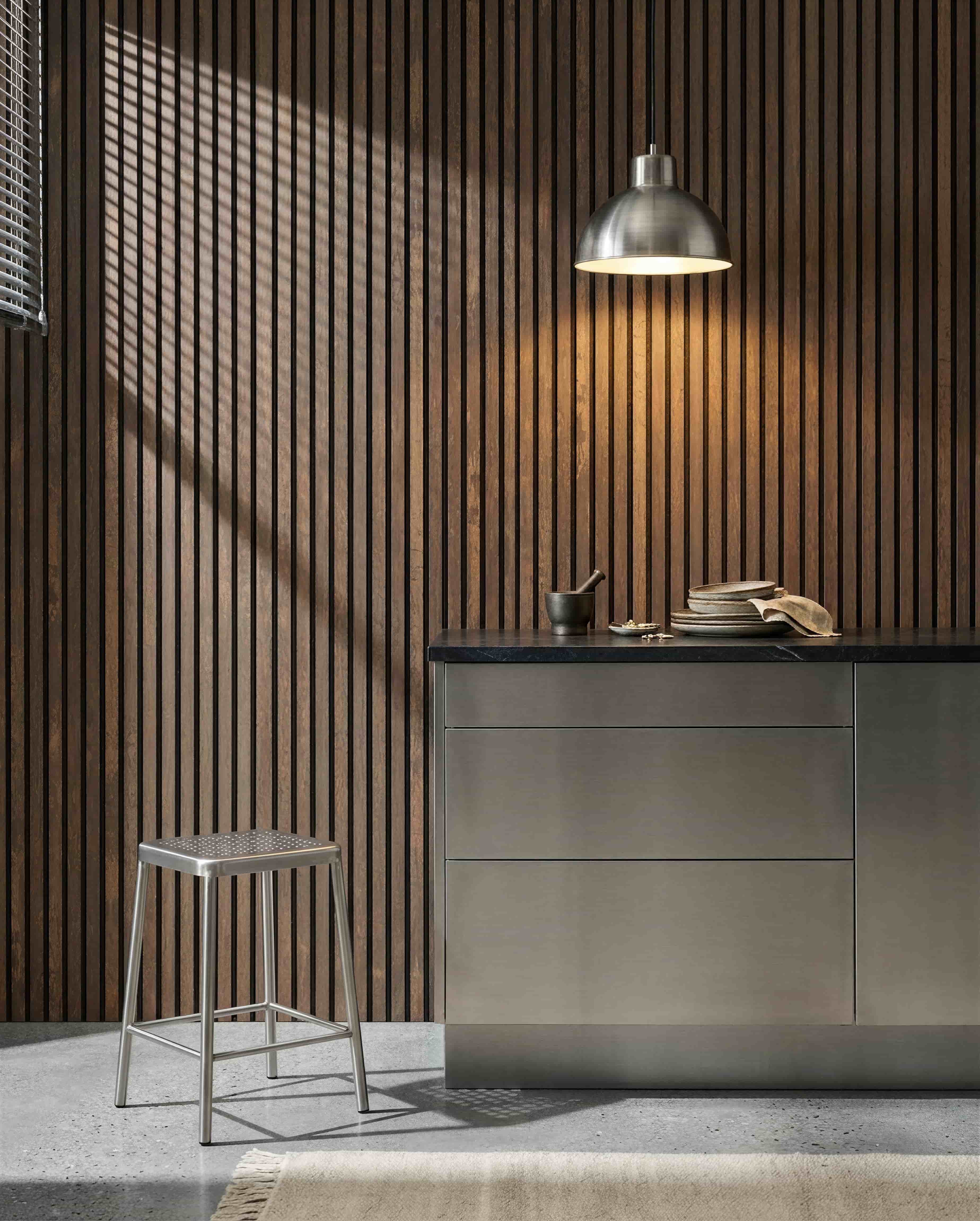 Keuken met een WoodUpp Akupanel Oxide Copper akoestische lattenwand, een roestvrijstalen werkblad, metalen kruk, hanglamp, assorted dishes, en vijzel met stamper.