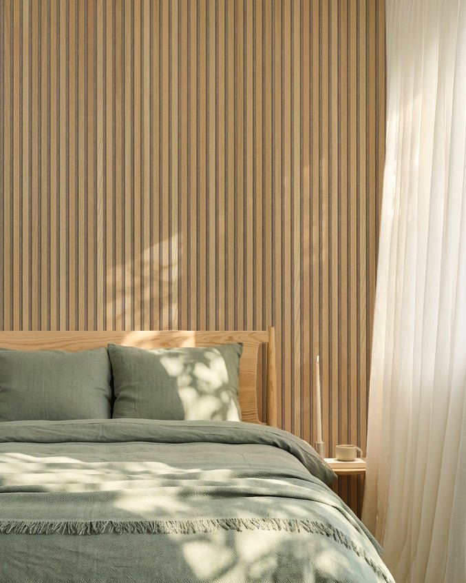 Minimalistische Scandinavische slaapkamer met een WoodUpp Akupanel eiken Akoestisch paneel wand, saliegroen beddengoed, een houten bedframe en transparante witte gordijnen.