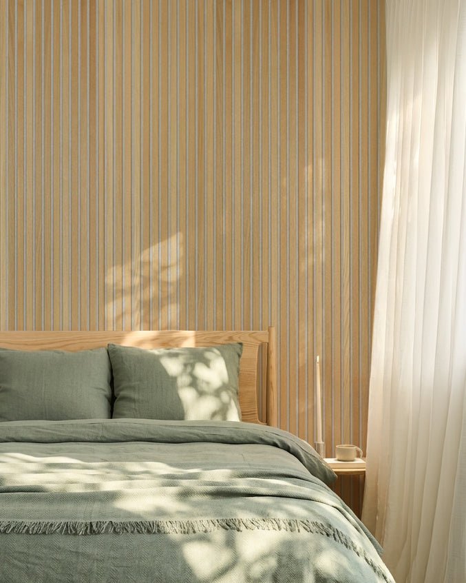 Minimalistische Scandinavische slaapkamer met saliegroen beddengoed en een WoodUpp Classic Oak Akupanel akoestische lattenwand; zonlicht zorgt voor zachte schaduwen op het bed.