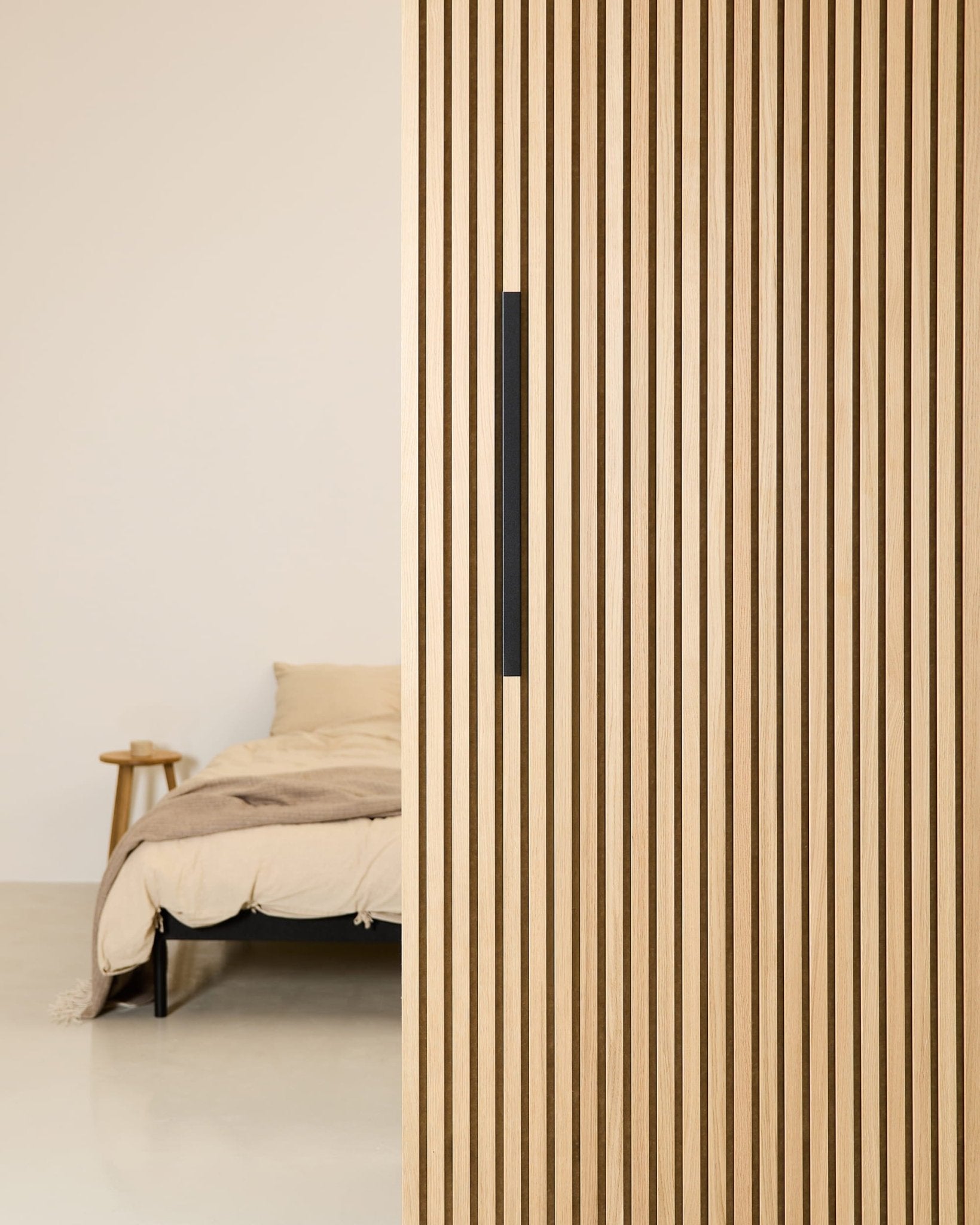 Chambre à coucher minimaliste avec un lit beige, partiellement dissimulé par une cloison de séparation WoodUpp EMBRACE en aluminium noir de 60 cm, dotée dune poignée noire.