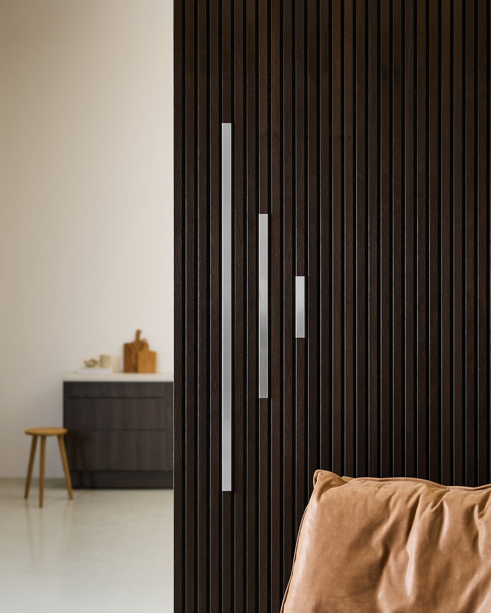 Minimalistisch interieur met een Akoestisch paneel wand van donker hout, WoodUpp Liva cover in gepolijst steel (20 cm), een zandkleurig kussen en moderne meubels.