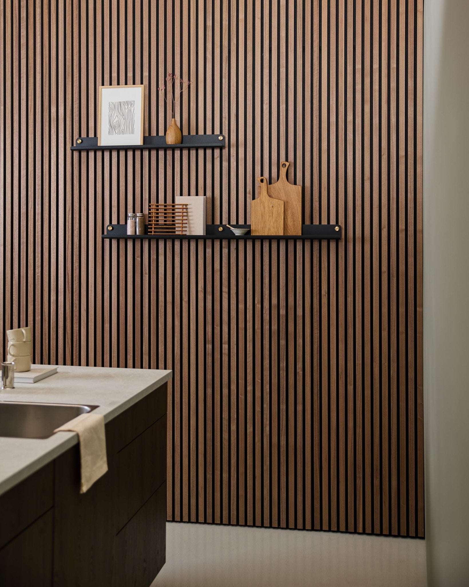 Moderne keuken met een akoestisch lattenwandpaneel in Scandinavische stijl, een black WoodUpp Norr Narrow Shelf (115,9 cm) voor decoratie, en een handdoek over de gootsteen gedrapeerd.