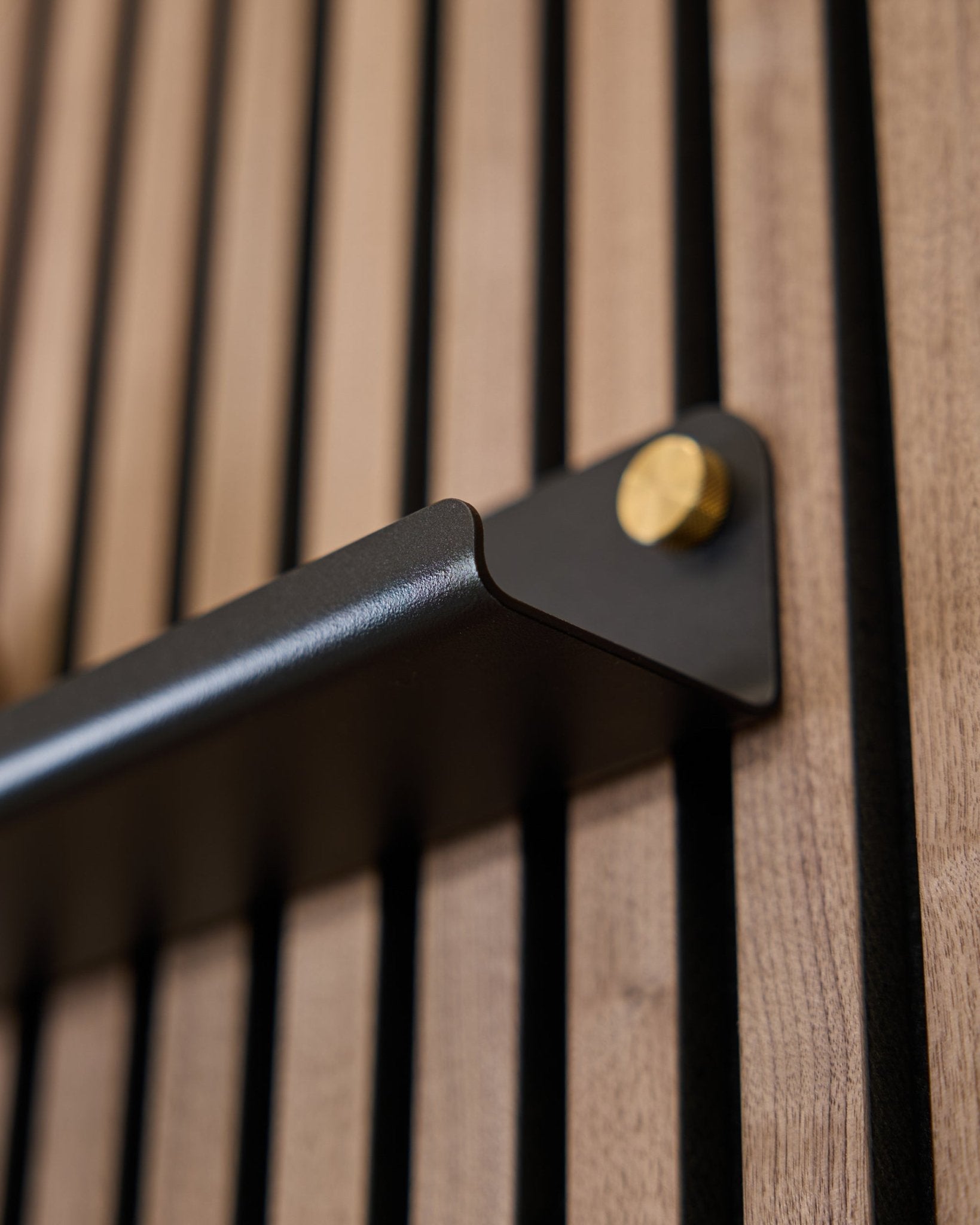 Close-up van de Norr | Narrow Shelf (75.9 cm) van WoodUpp in black, met een steel greep met gouden bouten en een verticaal gegroefd akoestisch oppervlak.