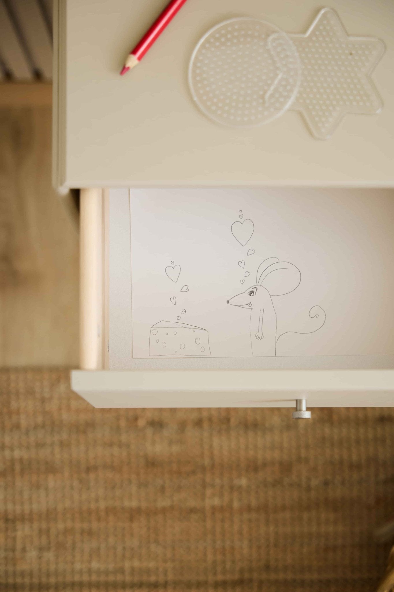 Een muis en kaas met hartjesmotief sieren een beige WoodUpp Arka-ladekast; een rood potlood en pegboards liggen op het bijpassende tafelblad erboven.