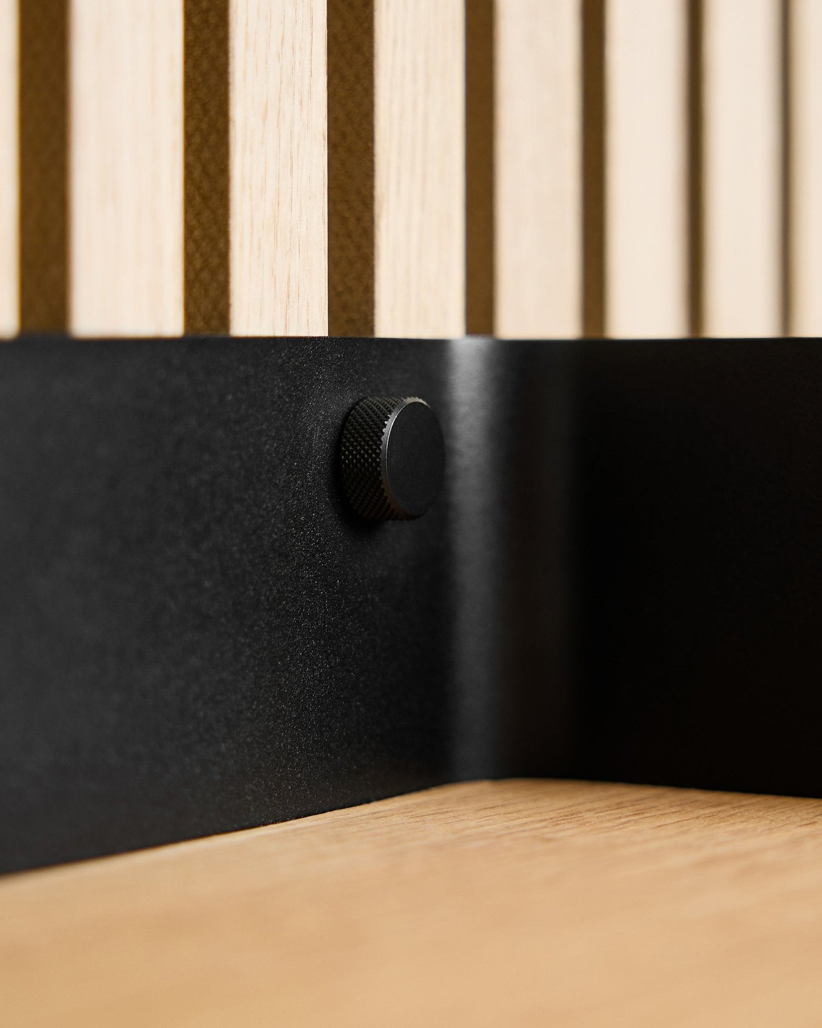 Gros plan sur deux vis WoodUpp Finger black (M5x10 mm, 20x8.8) avec des vis brass, posées sur un mur acoustique à lattes en bois nordique et une surface en bois clair.