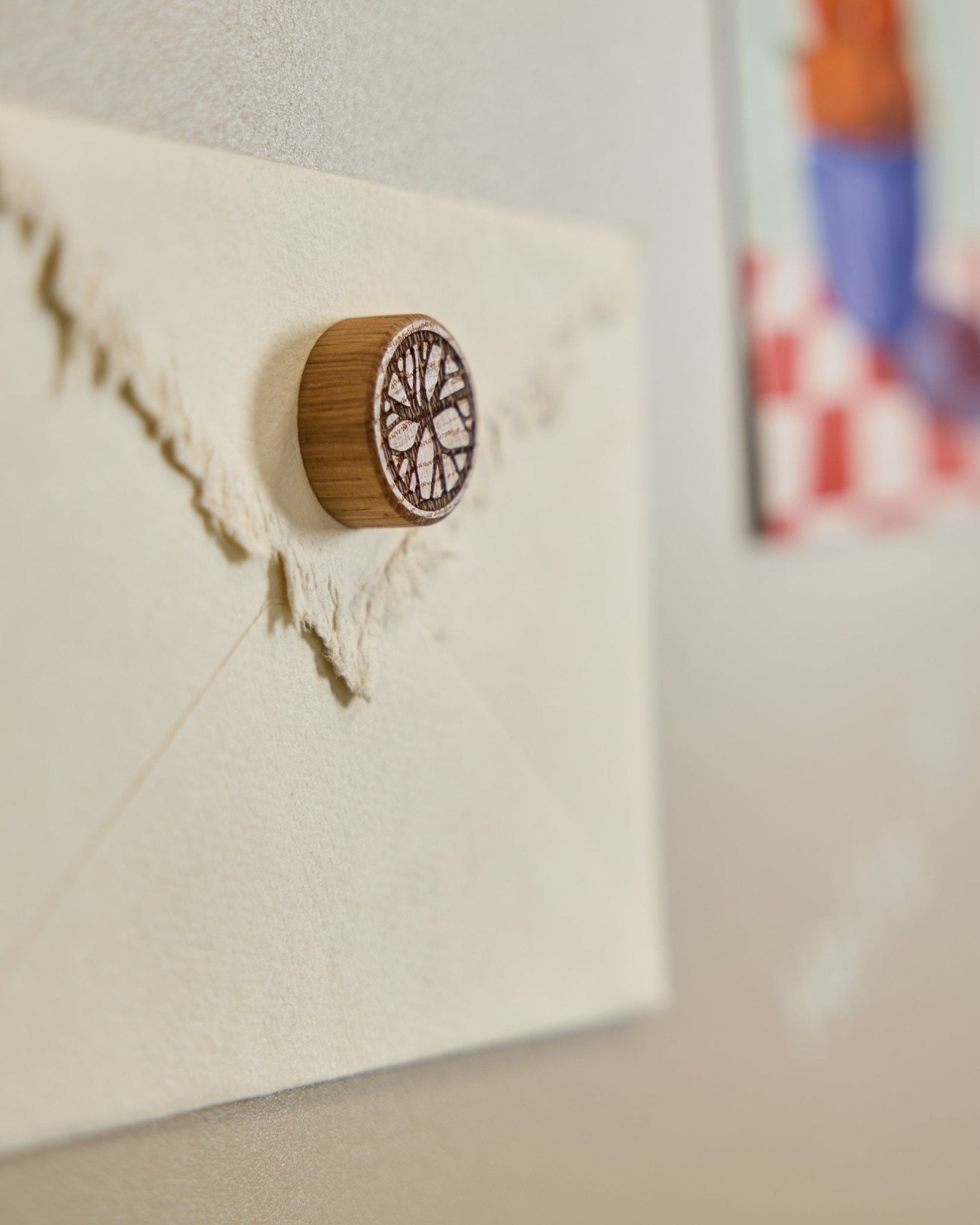 Een crèmekleurige envelop is met een Norr Natural Oak magneet van WoodUpp op een Akoestisch paneel bevestigd, met een minimalistisch boomontwerp.