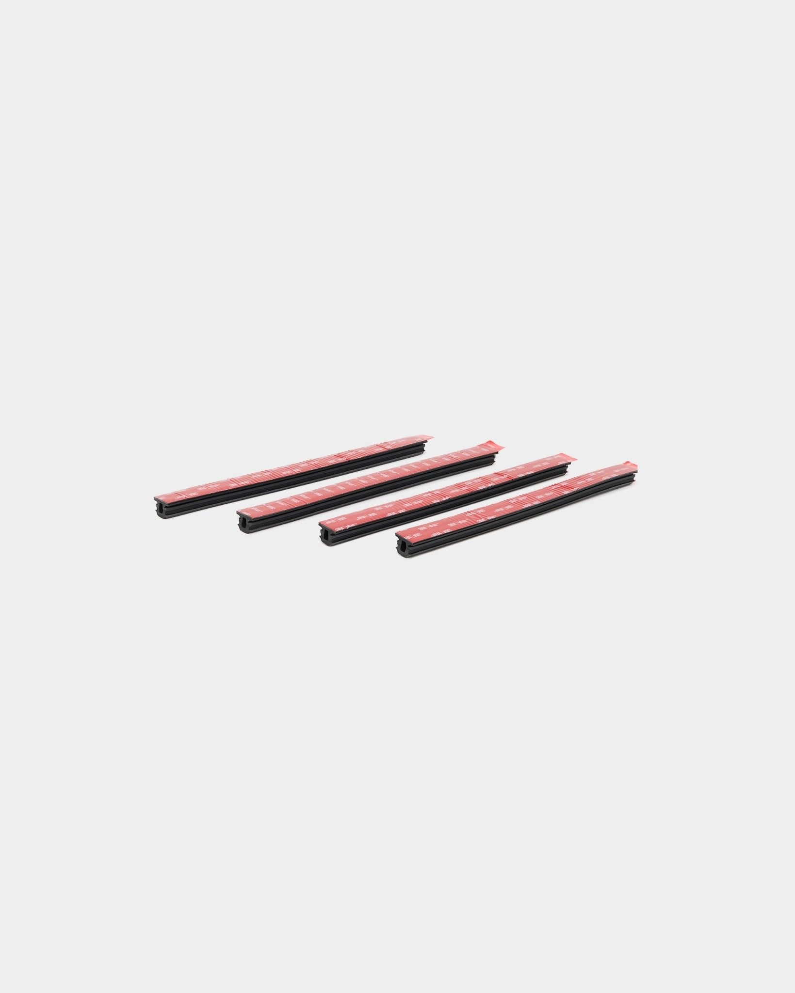 Vier black Dupps Pop-on Profile beschermstrips voor autodeurranden, WoodUpp 4-delige set, diagonaal geplaatst op een witte achtergrond.
