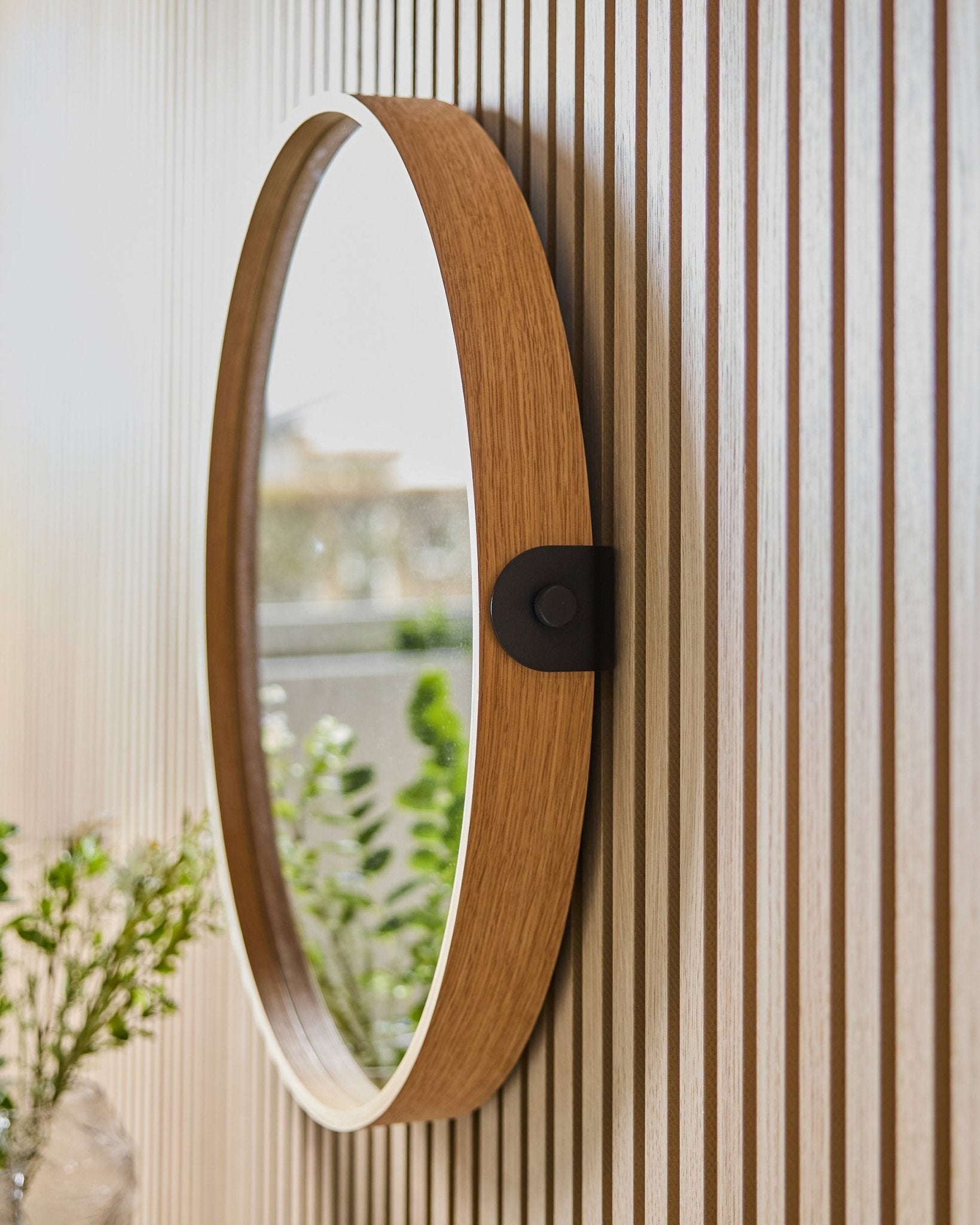 Linn | Mirror / Natural Oak van WoodUpp, gemonteerd op een gestreepte Akoestisch paneel wand, waarin groen en natuurlijk licht van een nabijgelegen raam worden weerspiegeld.