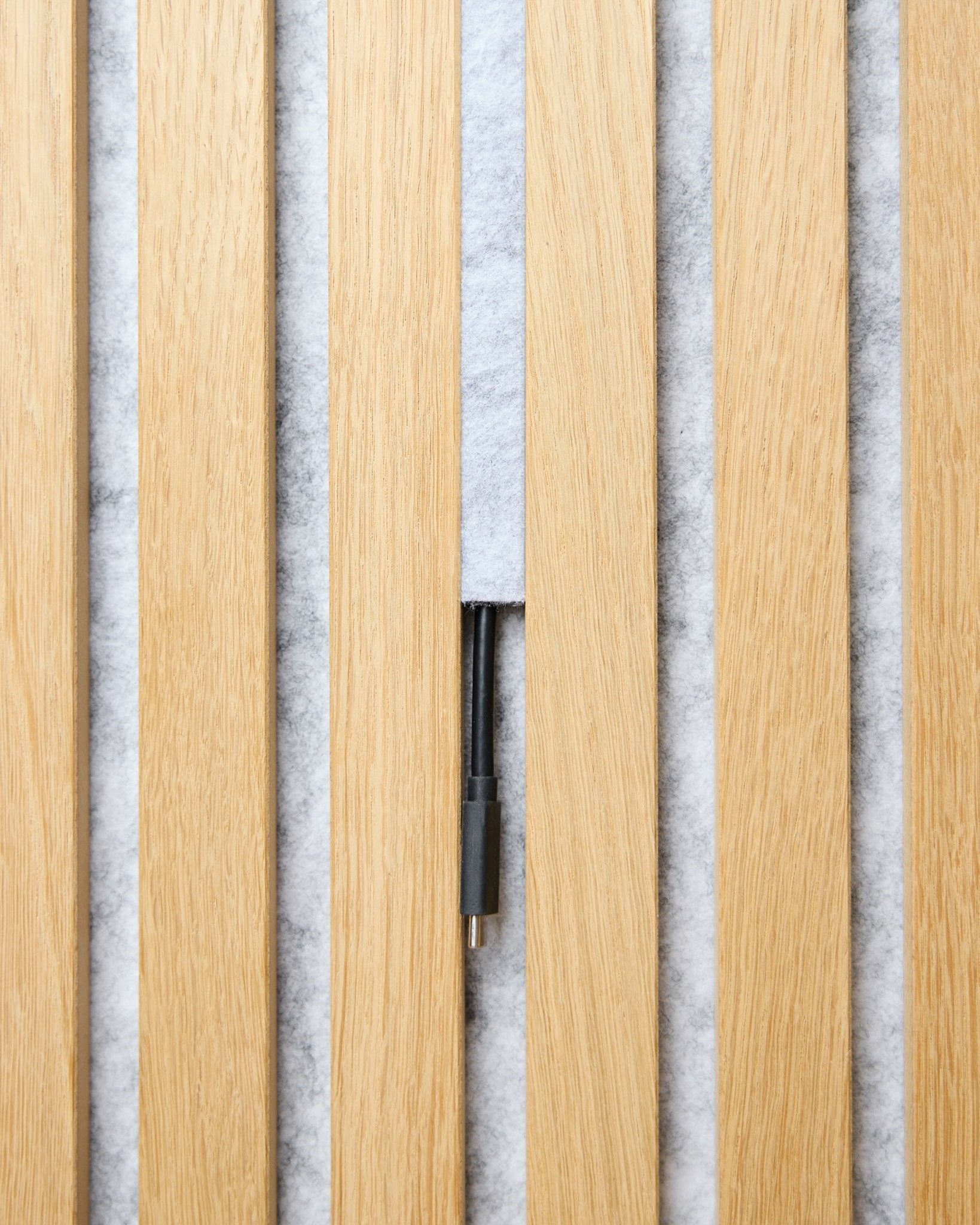 Le lot de cache-câbles Pop-on Dupps (grey, 3 pcs) de WoodUpp organise les câbles entre des lattes acoustiques en bois clair Akupanel, sur un fond blanc texturé.