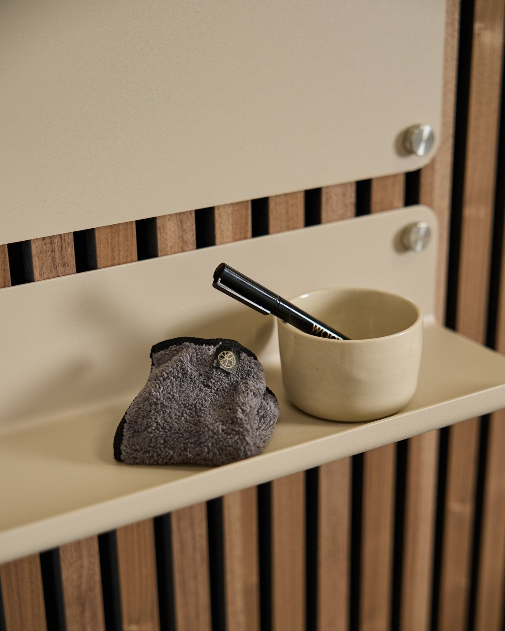 Le set Blackboard WoodUpp Norr comprend une tasse small beige, une brosse à manche black et un chiffon de nettoyage, posés sur une étagère beige avec un panneau acoustique en bois de style nordique.