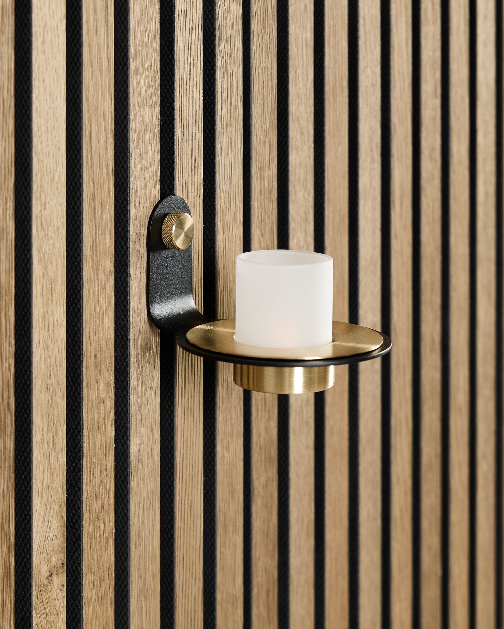Le bougeoir Norr en black et brass de WoodUpp est monté sur un panneau acoustique en bois nordique Akupanel, avec des lattes black vertical.
