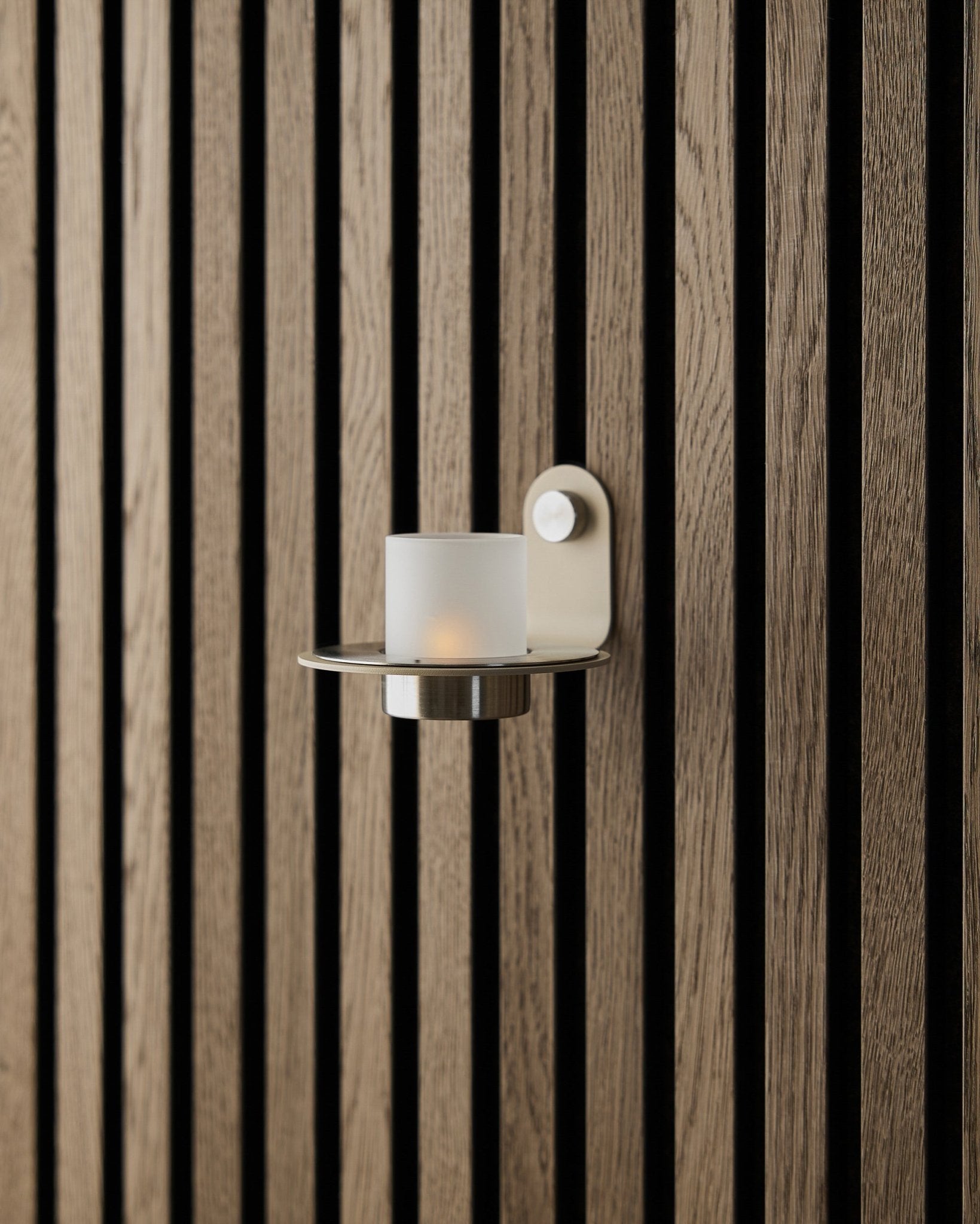 De Norr Candle Holder in beige roestvrij steel van WoodUpp, gepresenteerd op een beige Akupanel Akoestisch paneel wand.