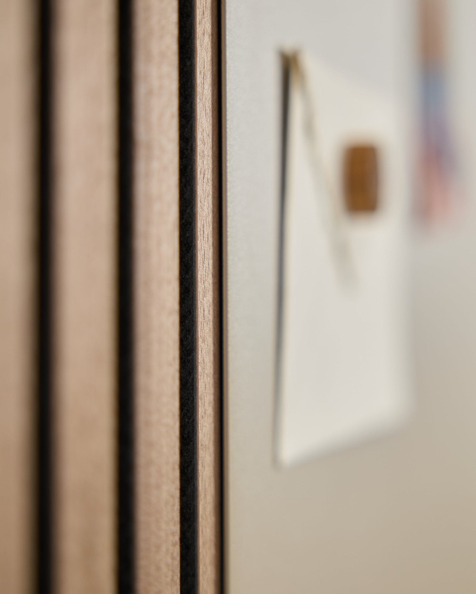 Gros plan sur un panneau acoustique en bois WoodUpp Akupanel avec des lattes vertical, à côté d’un tableau magnétique Norr large beige flou en arrière-plan.