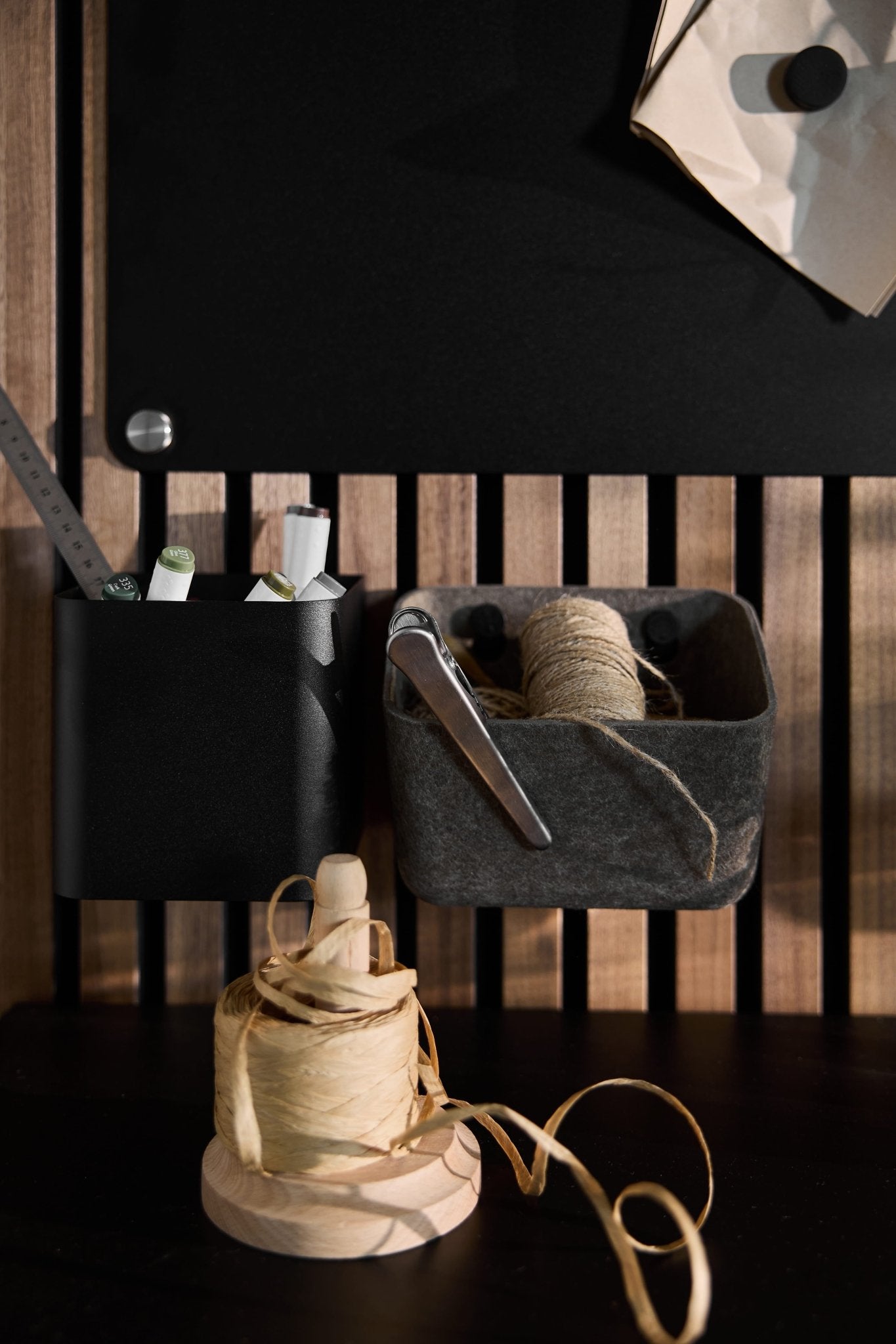 Les rangements en feutre gris foncé « Luva » de WoodUpp permettent de ranger stylos, ciseaux et ficelle sur un panneau Akupanel en bois ; de la ficelle supplémentaire est rangée en dessous.