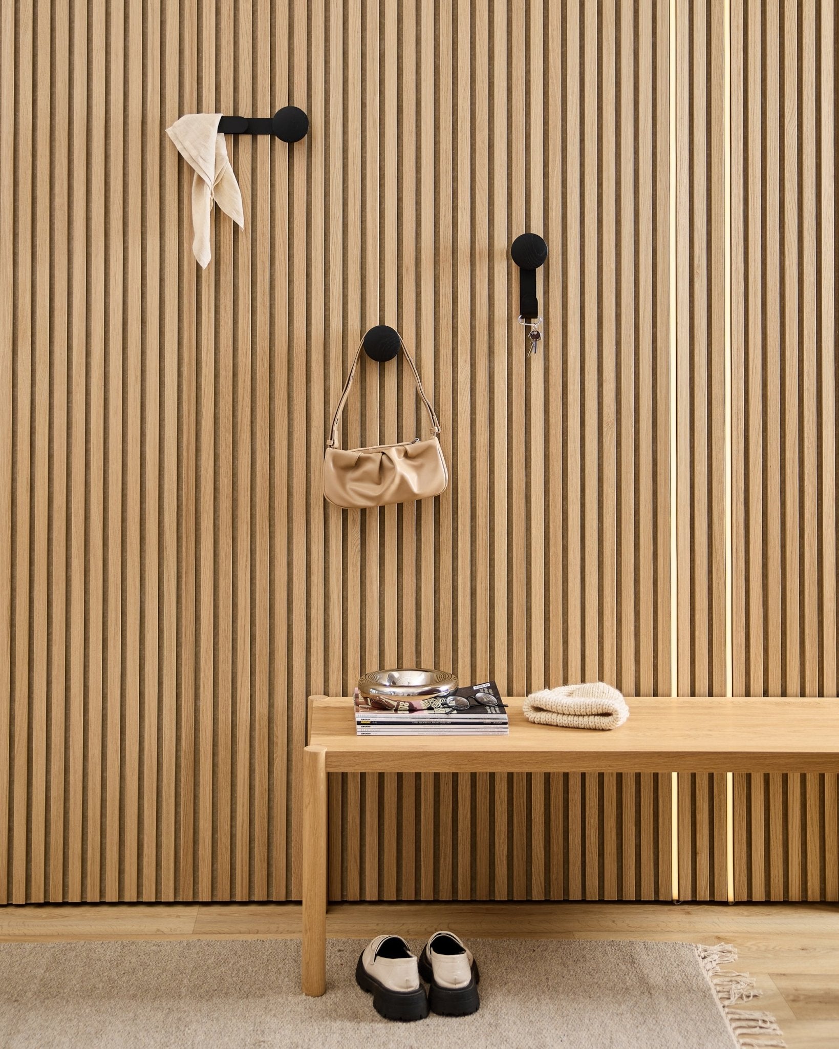 Minimalistische hal met een WoodUpp Linn Horizontal Hanger in Black Oak met black haken, een houten bankje, schoenen, boeken en een schaaltje. Scandinavische stijl.