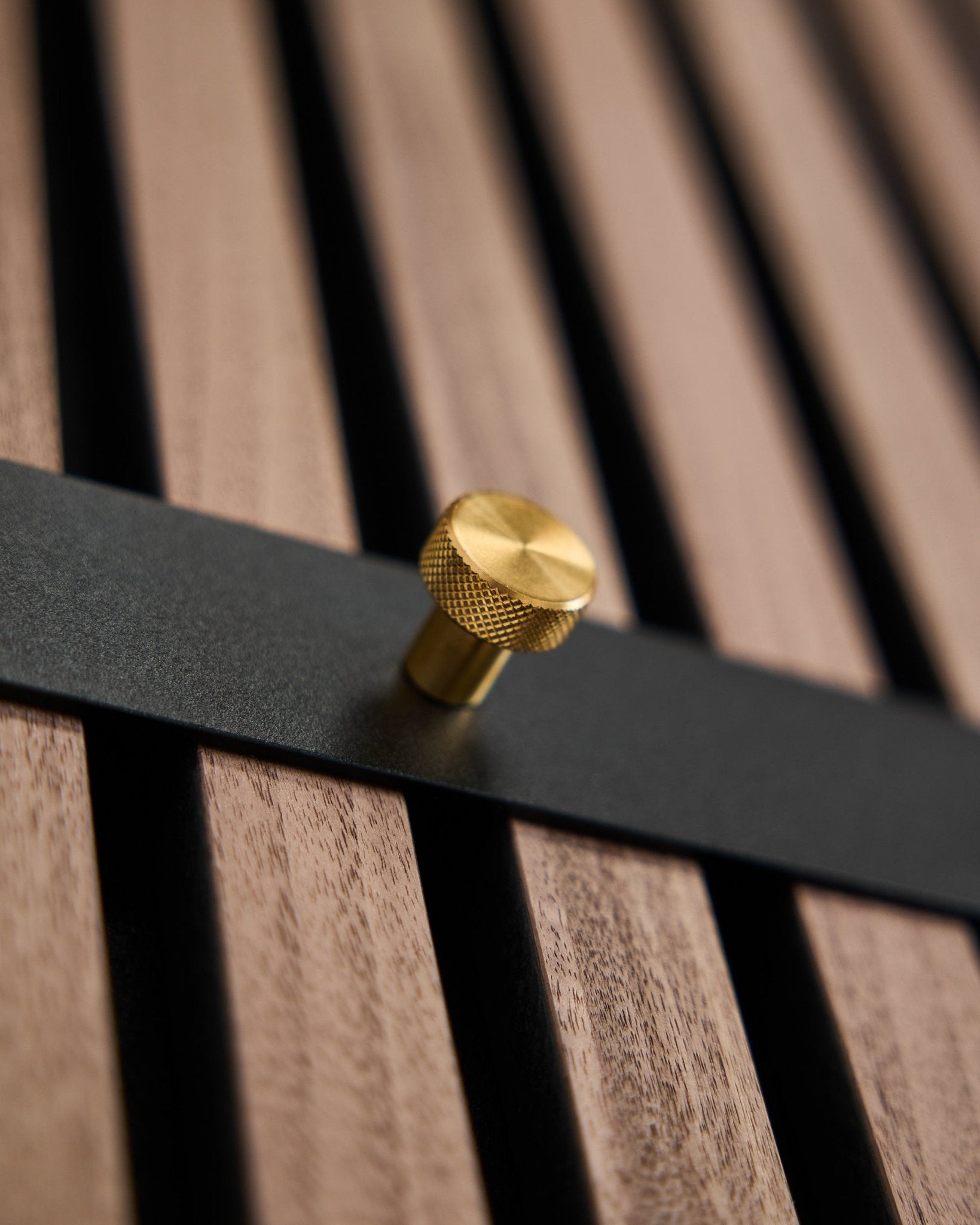 De WoodUpp Norr kapstok heeft zeven black haken met brass knoppen, gemonteerd op een brown lattenwandpaneel, ontworpen als Scandinavisch accessoire voor Akupanel.