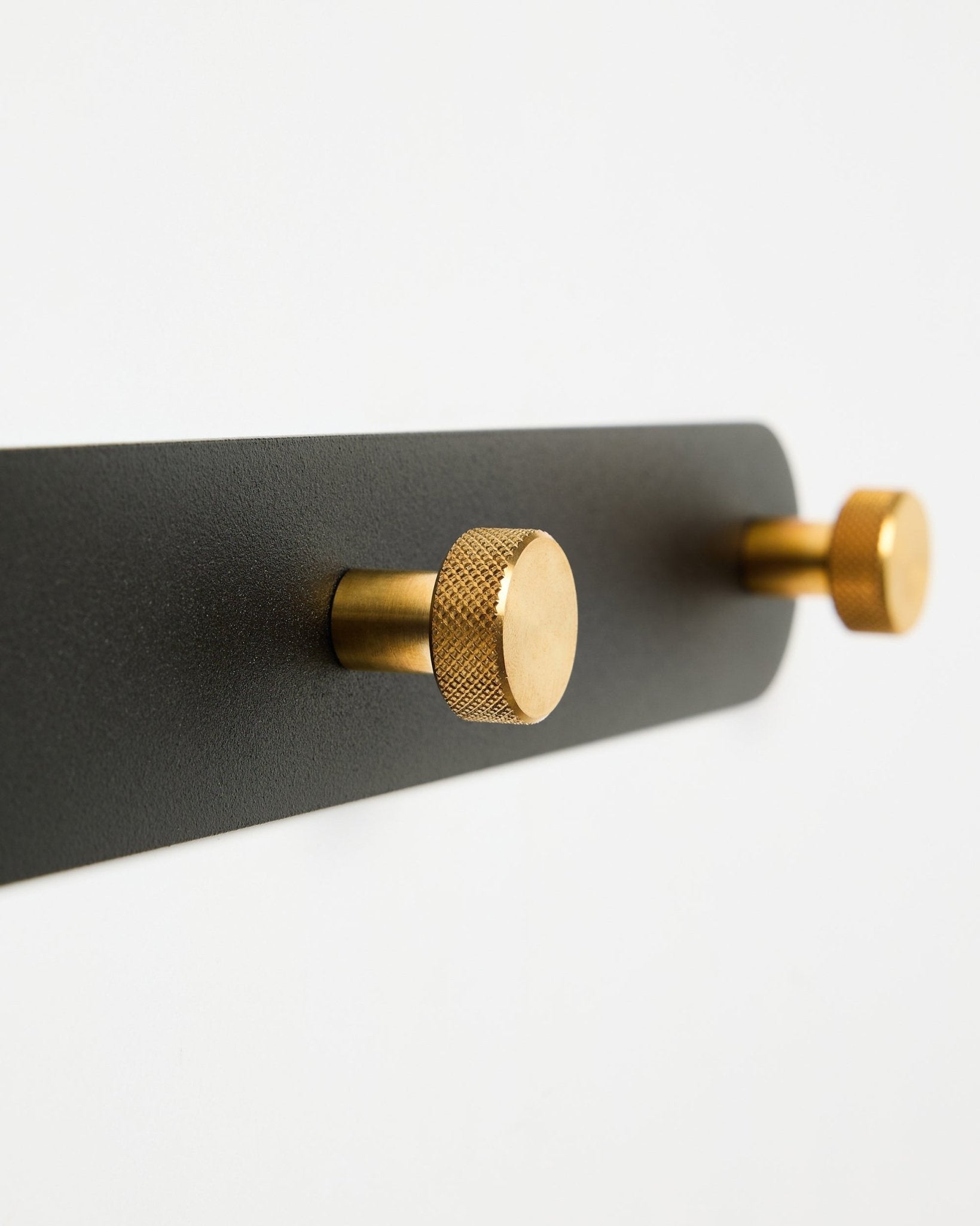 WoodUpp Norr kapstok, model X7, met twee cilindervormige black en brass haken op een black bevestiging, weergegeven tegen een witte achtergrond.