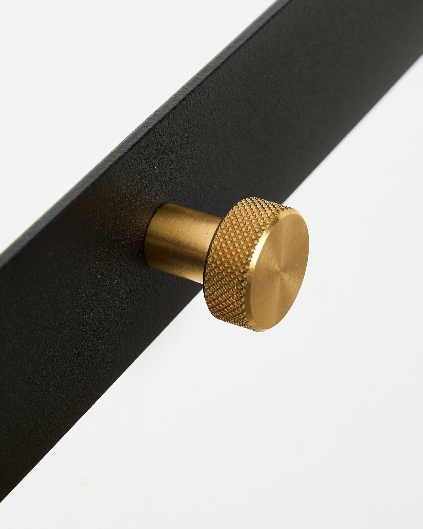 Close-up van de Norr Coat Hook Rack X5 van WoodUpp, met black gepoedercoat steel en ronde, getextureerde brass knoppen, tegen een witte achtergrond.