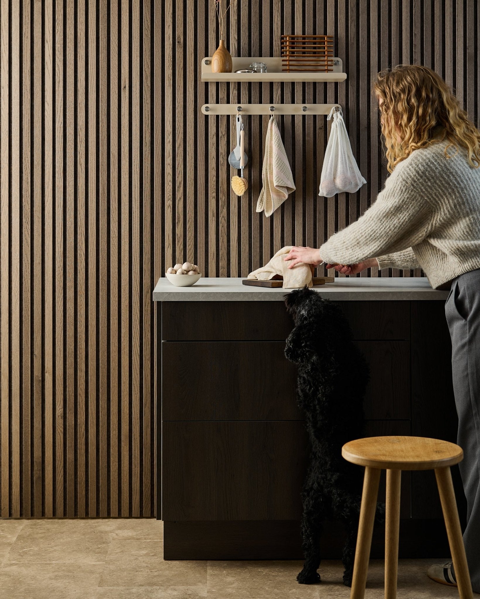 Een black hond staat op zijn achterpoten en reikt naar eten op een aanrecht, met Nordic akoestische houten panelen en planken op de achtergrond.