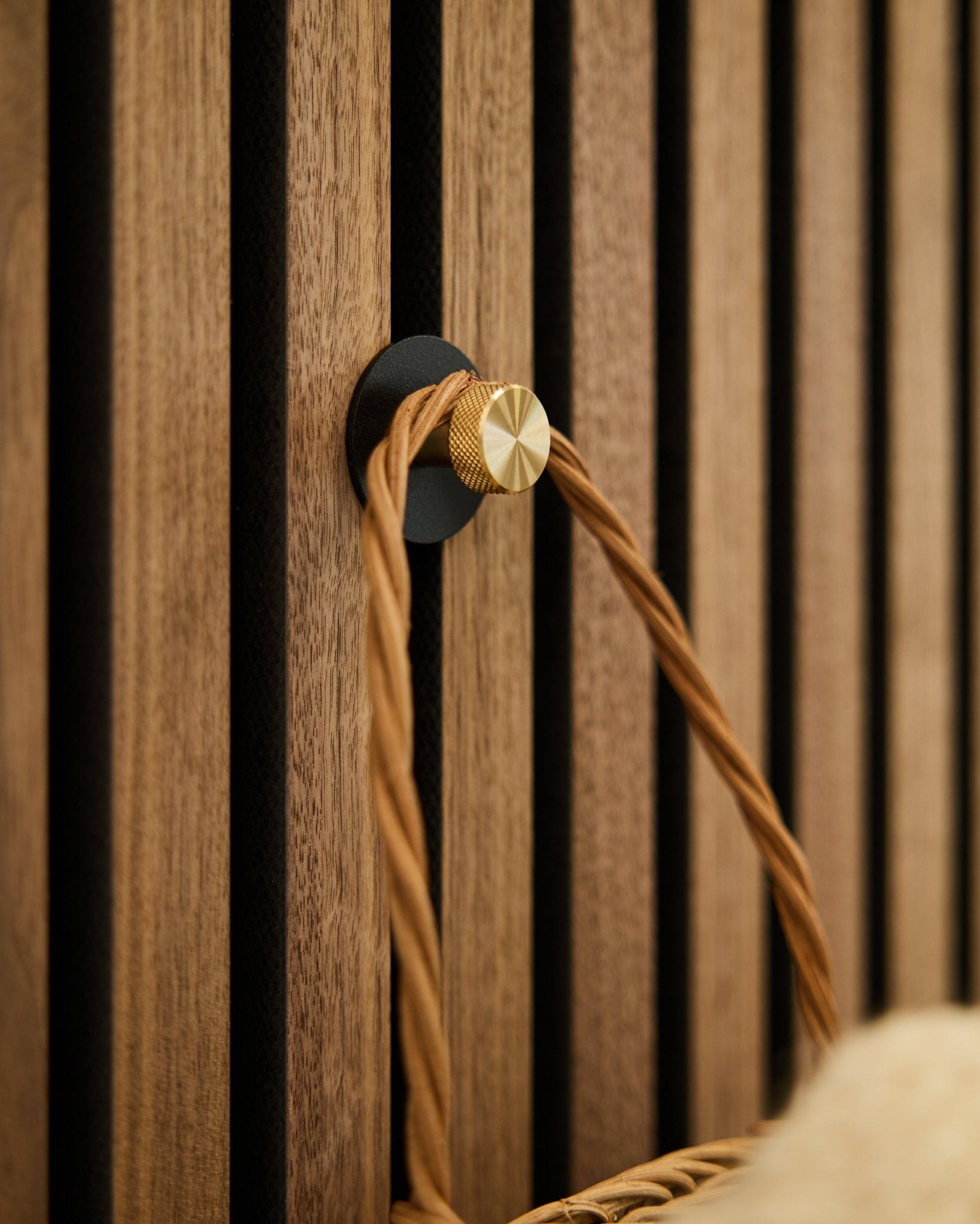 Patère WoodUpp Norr en black et brass, montée sur un Panneau acoustique en bois Akupanel, supporte une poignée tressée camel.