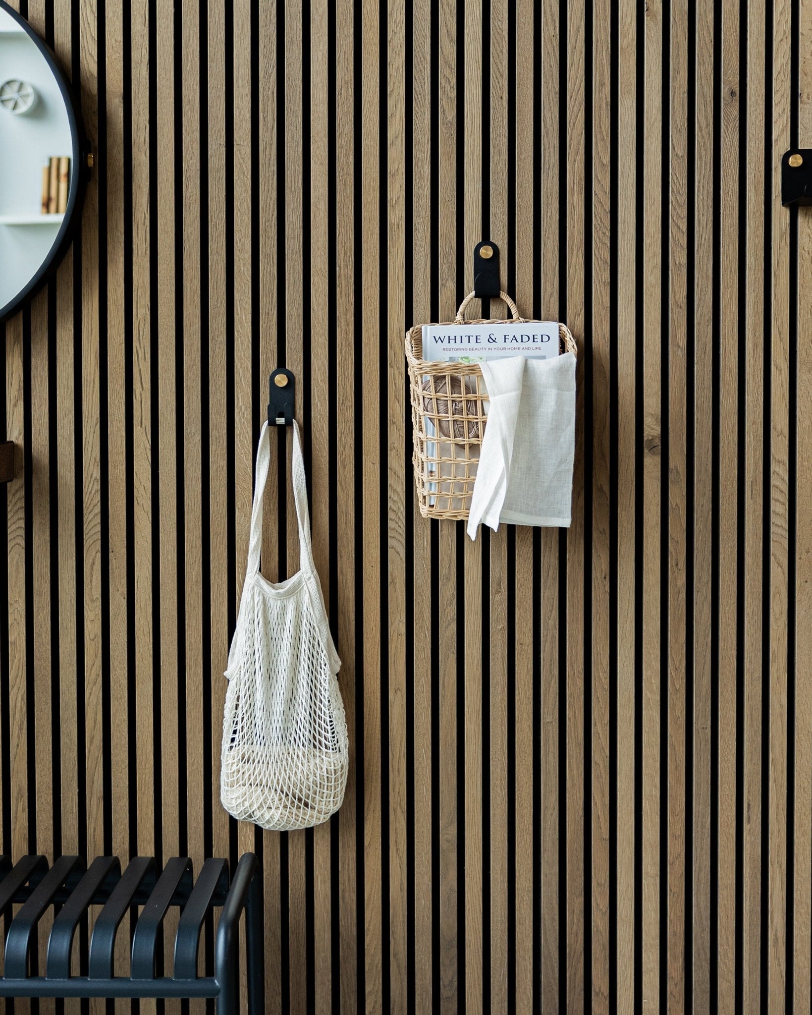 Een nettas en mand hangen aan Norr Single Hangers van WoodUpp op een Nordic houten Akupanel Akoestisch paneel; links is een deel van een spiegel zichtbaar.