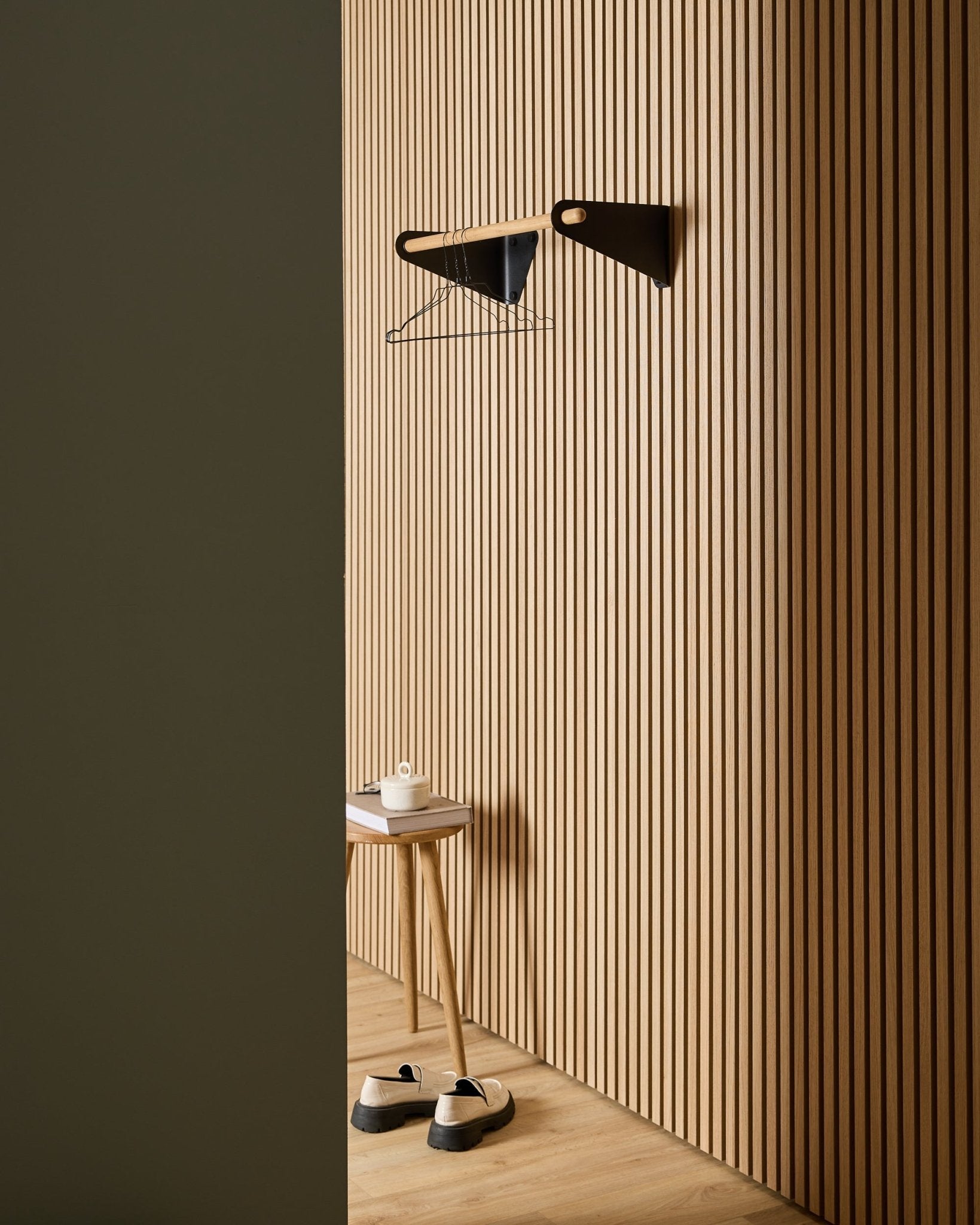 Minimalistische hal met WoodUpp Akupanel Nordic akoestische houten lattenwandpanelen, black Linn Coat Rail (75,9 cm), kruk, schoenen, wandplank en papierrol.