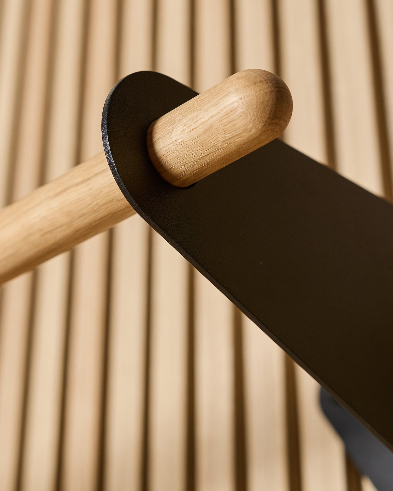 Close-up van de WoodUpp Linn Coat Rail in black, 75,9 cm, met een massief eiken stang gemonteerd in een black metalen beugel op een Nordic akoestisch lattenwandpaneel.