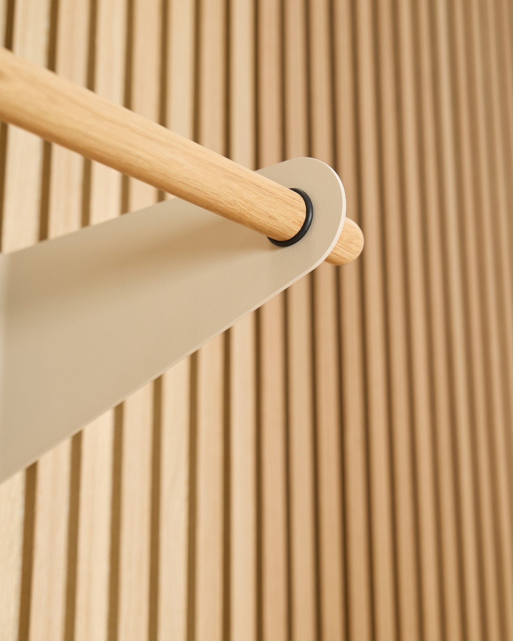 Close-up van de WoodUpp Linn kapstokrail in beige (75,9 cm), gemonteerd op een beige metalen beugel tegen een akoestisch lattenwandpaneel in Akupanel met textuur.