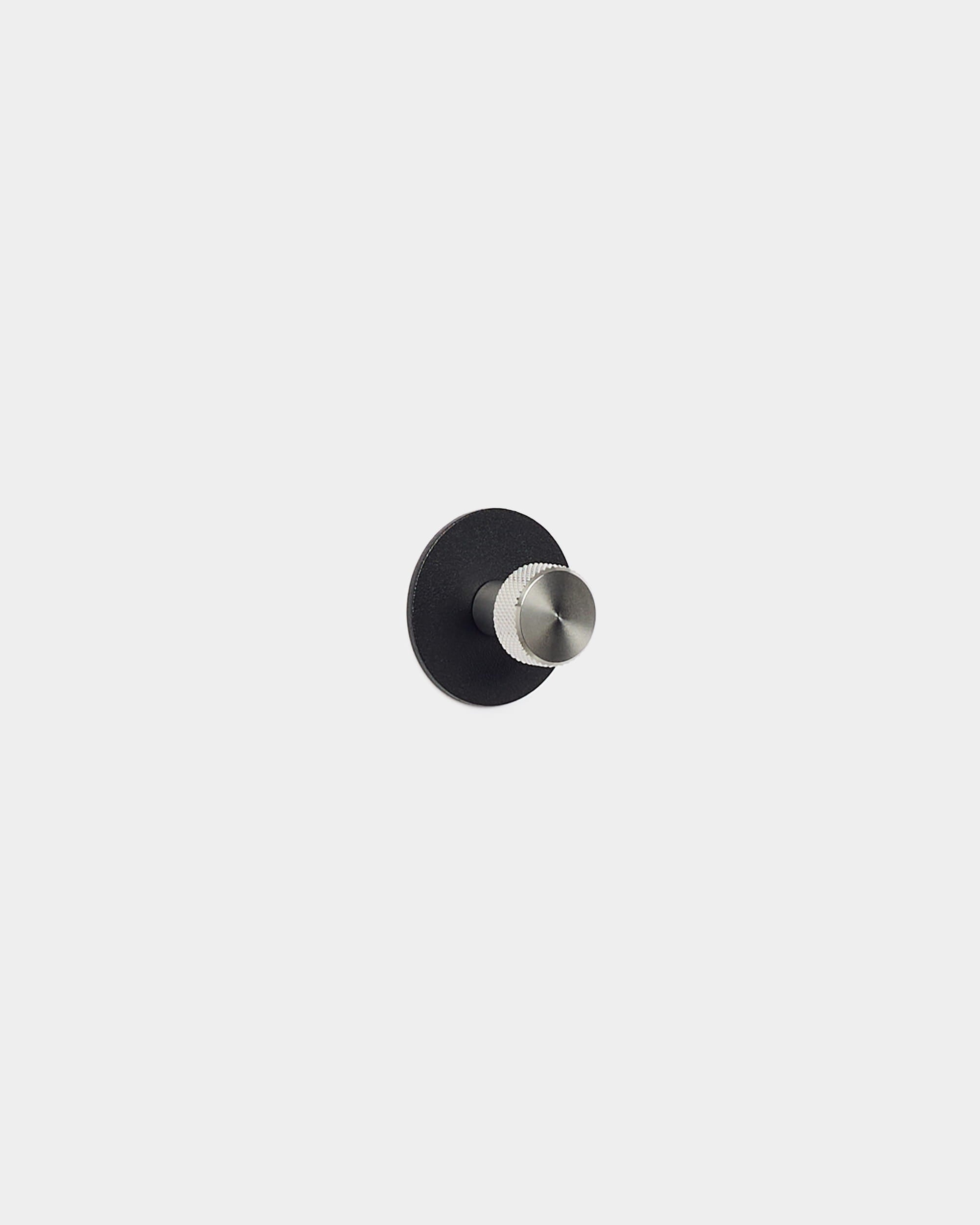 De Norr kapstokhaak van WoodUpp heeft een ronde basis van black en een zilverkleurige haak, ontworpen als accessoire voor Akupanel akoestische panelen — past perfect in minimalistische, Scandinavische interieurs.