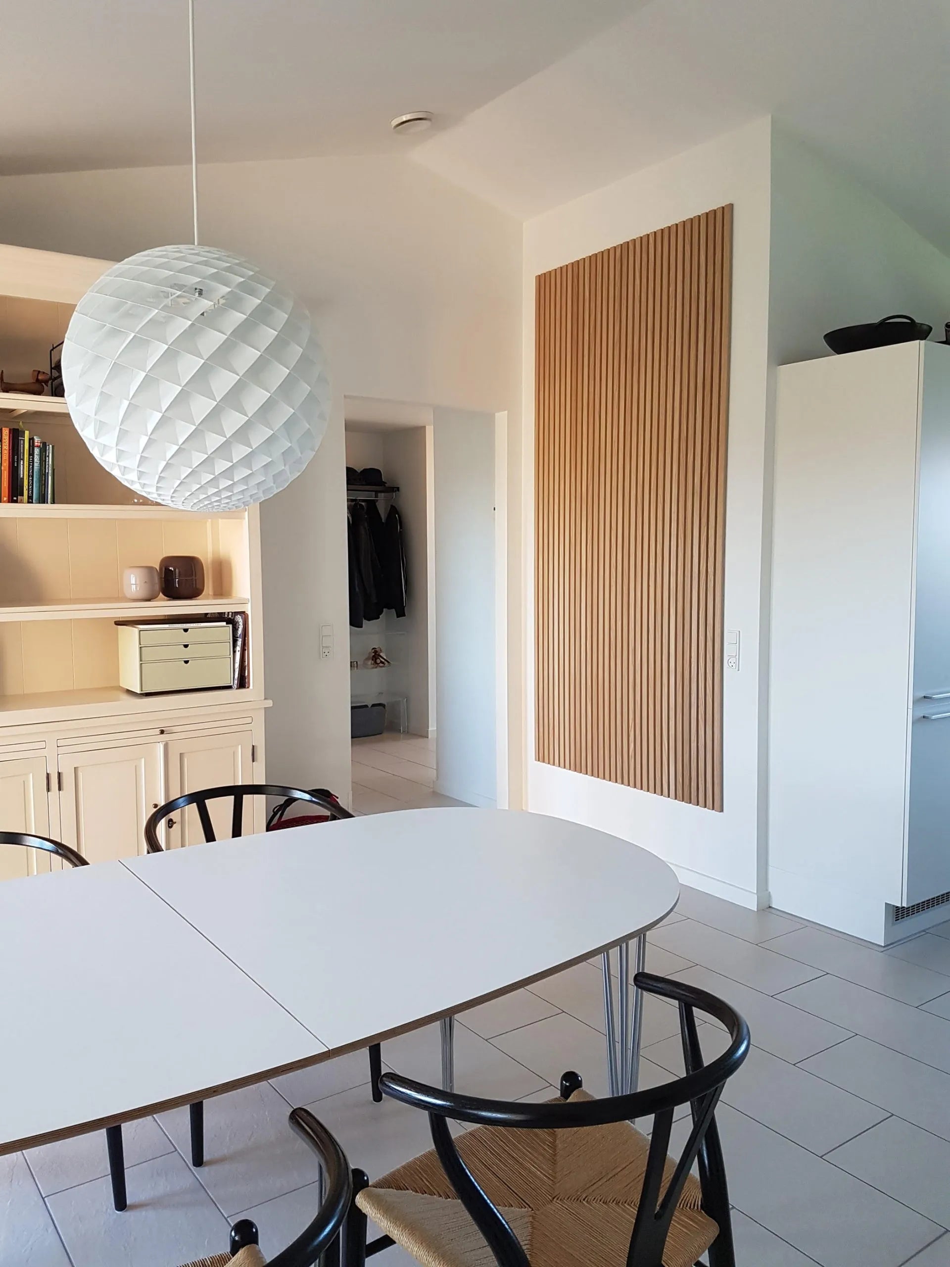 Moderne eethoek met een witte ovale tafel, zwarte stoelen, grote hanglamp met structuur en strakke lichthouten Akupanel akoestische kasten.