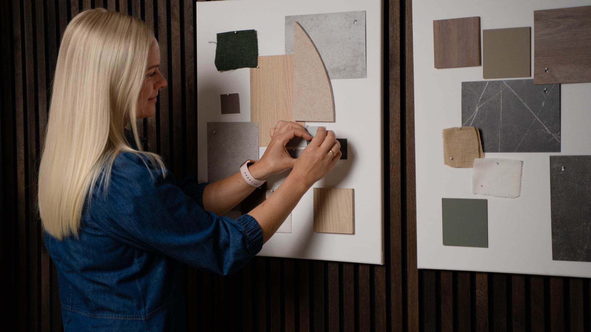 Een vrouw rangschikt stof- en kleurstalen op een moodboard, met een ander inspiratiebord naast haar, naast akoestische houten panelen uit de Akupanel-collectie van WoodUpp.