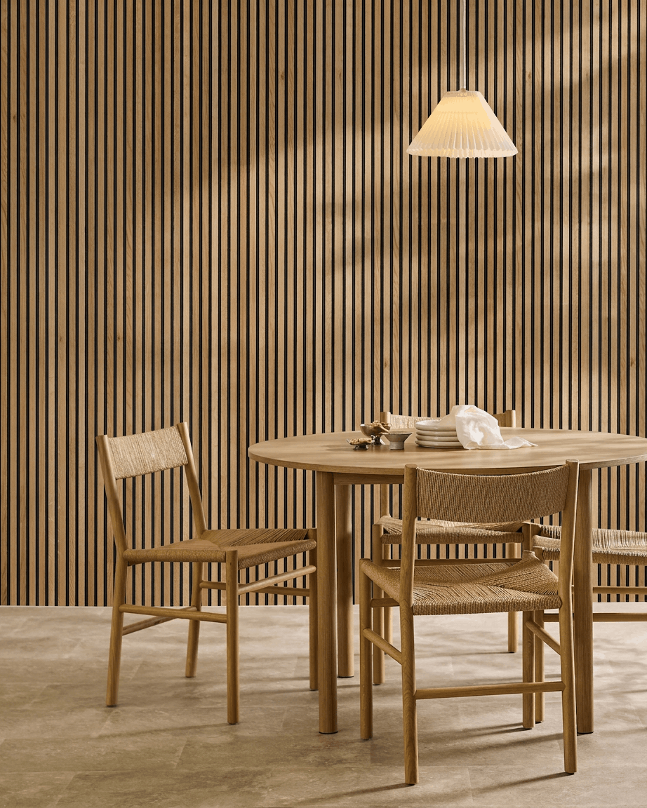 Minimalistische eethoek met een houten tafel, twee stoelen en een WoodUpp Akupanel akoestisch houten paneel in Rustic Brown Oak (300x60 cm), verlicht door een hanglamp.
