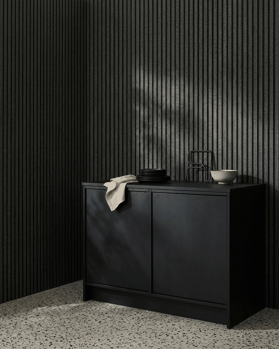 Een black kast naast een WoodUpp Akupanel akoestisch houten paneel in Charcoal/Black Felt, met kommen en borden erop, op een lichte terrazzovloer.