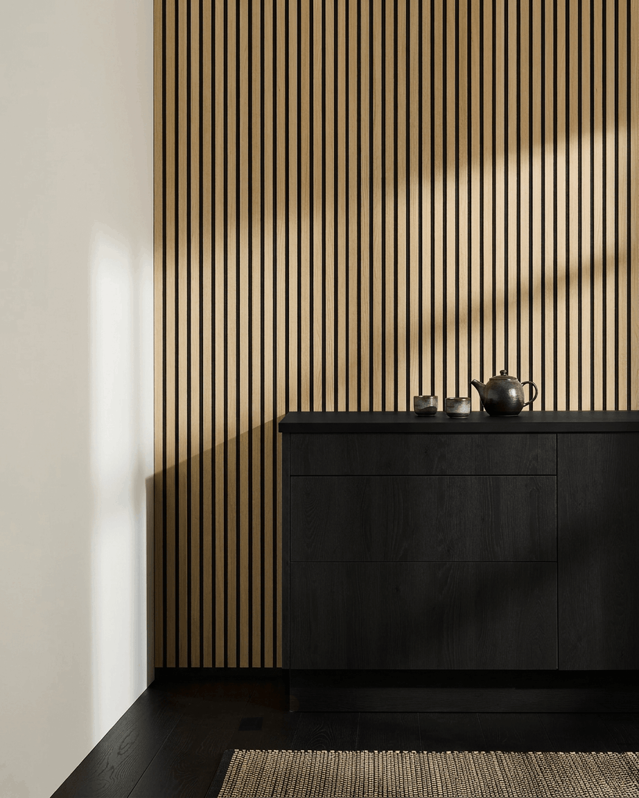 Minimalistische Scandinavische keuken met WoodUpp Akupanel Akoestisch paneel in Classic Oak, black kast, theepot, kopjes en geweven vloerkleed op een donkere houten vloer.