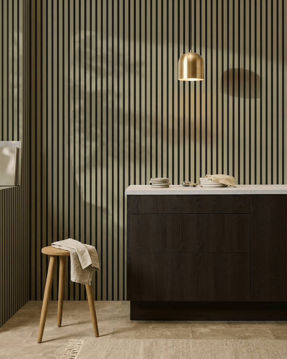 Cuisine moderne avec placards en bois foncé, plan de travail en marbre, suspension brass, et un panneau mural acoustique à lattes WoodUpp Akupanel Colored pour l’absorption acoustique.