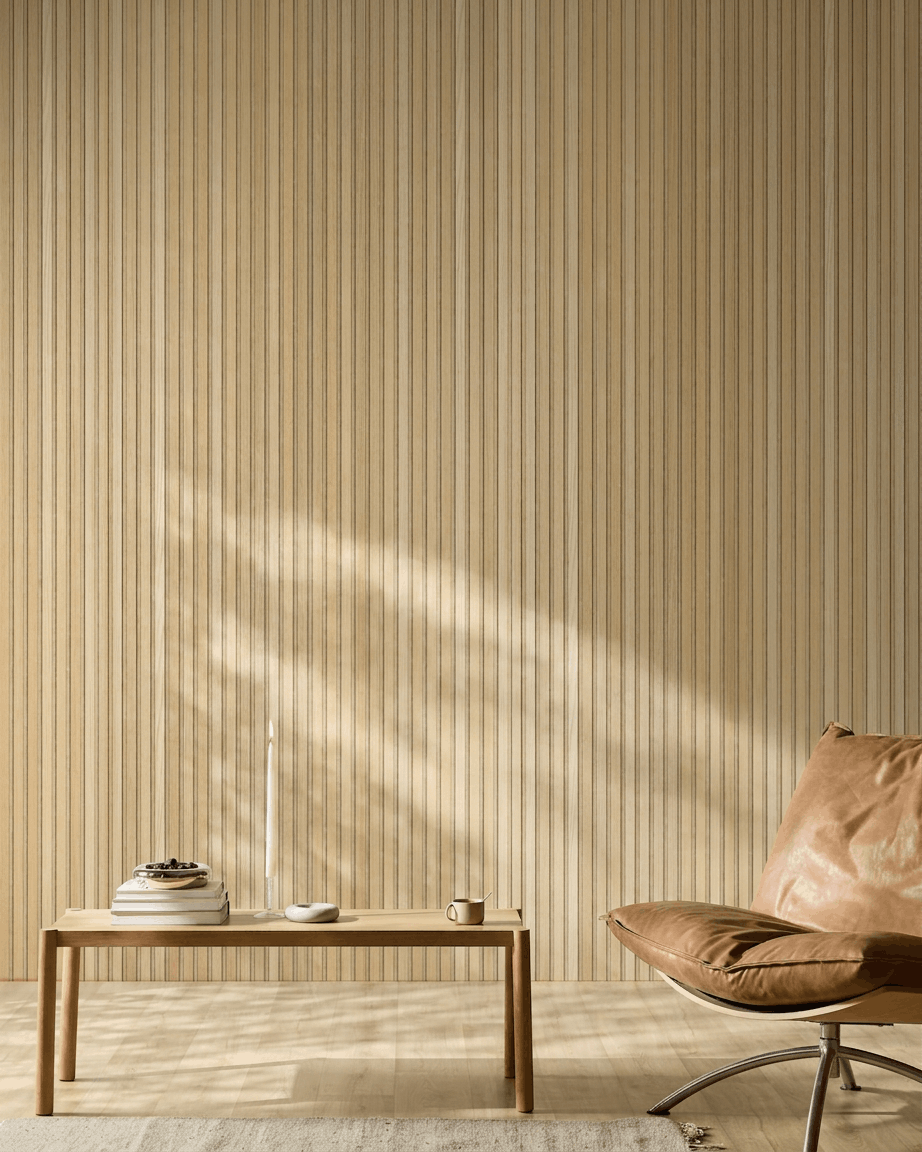 Pièce scandinave minimaliste avec un panneau acoustique en bois WoodUpp Akupanel en chêne classique Natural Wood, un fauteuil en cuir fauve et une table en bois sobre avec des touches chaleureuses.