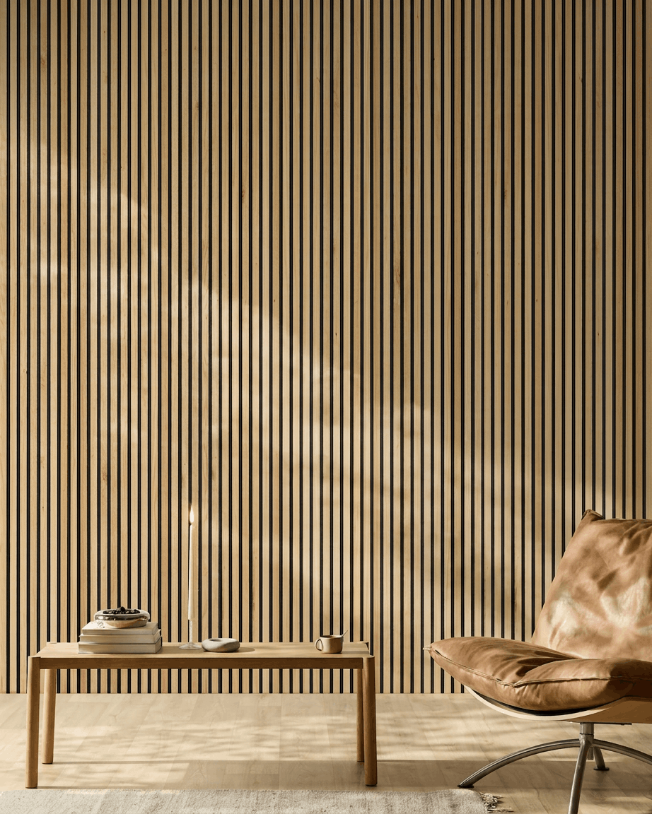Zonlicht verlicht een moderne ruimte met een WoodUpp Akupanel Akoestisch paneel in Rustic Natural Oak aan de muur, naast een cognackleurige leren stoel en een minimalistische bank.