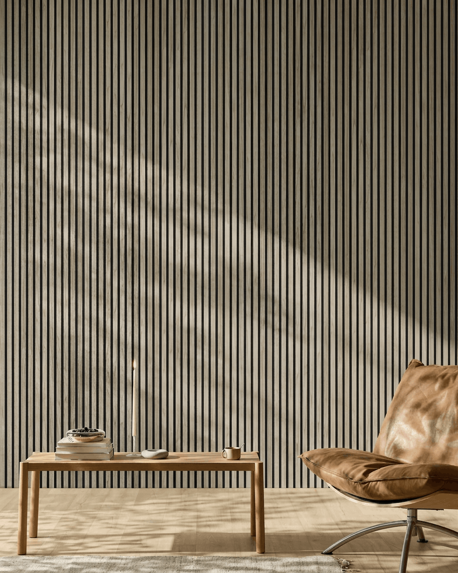 Pièce minimaliste avec un WoodUpp Akupanel 240x60 cm en chêne vieilli avec feutre black, un banc en bois, des livres, une bougie, une tasse et un fauteuil en cuir fauve.