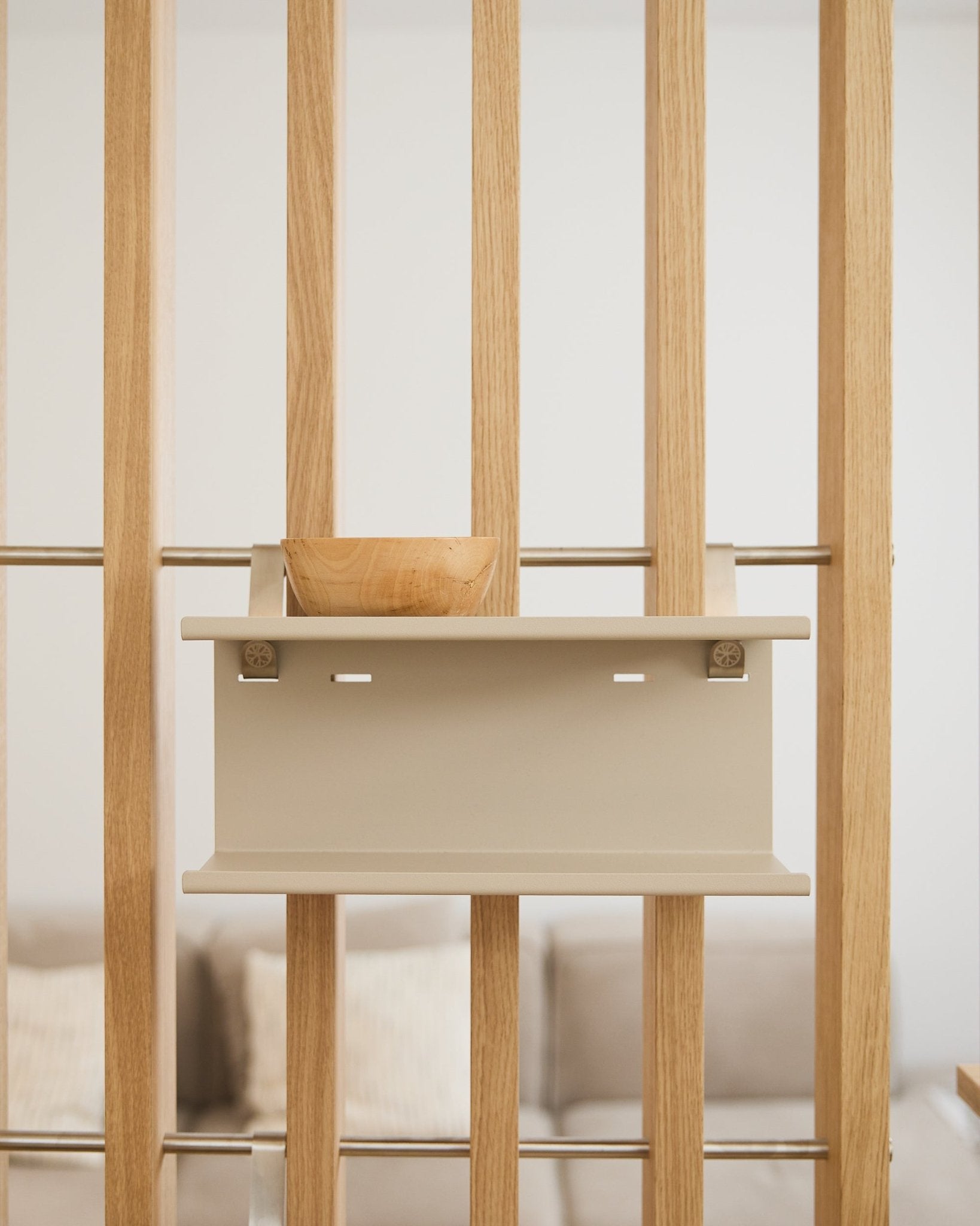 Een small houten kom op de beige Nell dubbele metalen plank van WoodUpp (31,7 cm), met een onscherpe bank en kussens op de achtergrond.