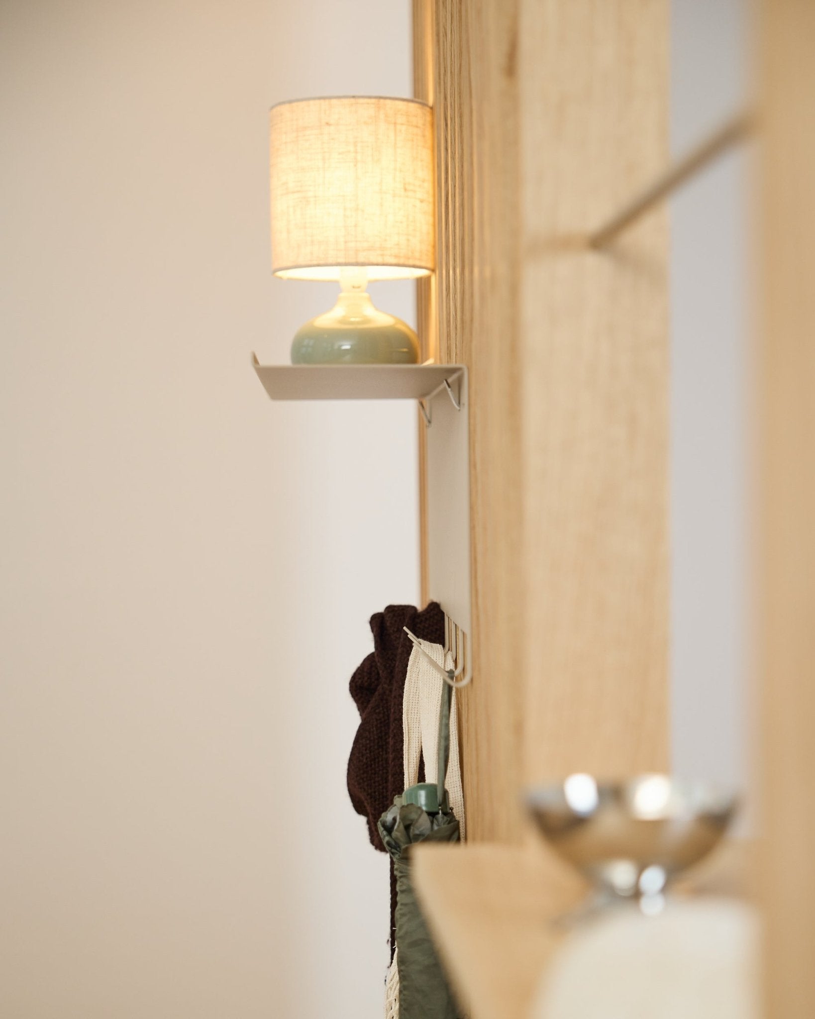 Een beige WoodUpp Nell kapstok BM1 (63,5 x 24 cm) staat onder een small tafellamp naast een wand van licht Scandinavisch hout Akoestisch paneel.