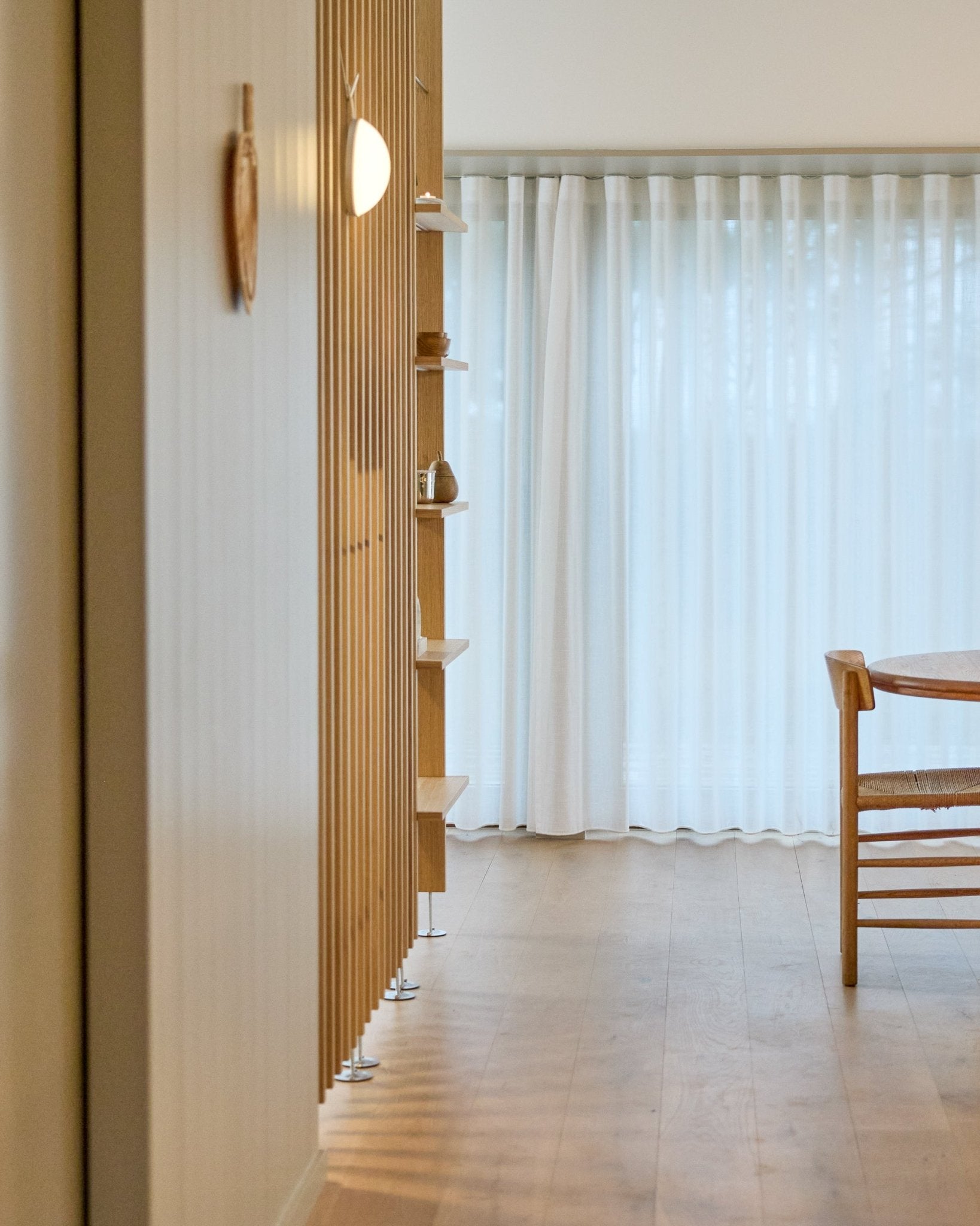 Minimalistische ruimte met een WoodUpp Embrace roomdivider van vloer tot plafond, houten vloer, planken, stoel en transparante gordijnen voor large ramen.