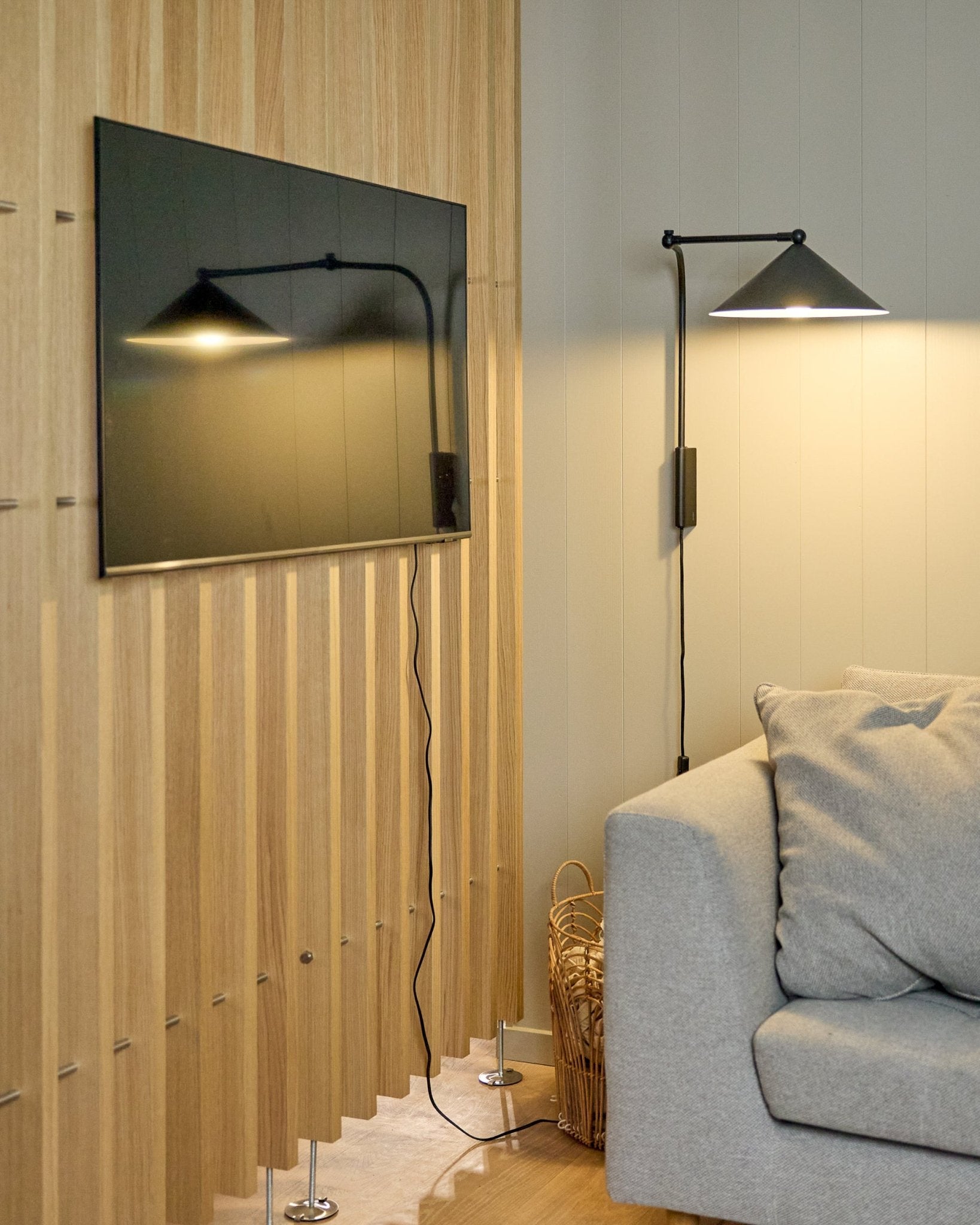 Een Nell | TV-Mount / BM1 van WoodUpp (Beige, 64x44 cm) bevestigt een flatscreen-tv op een Nordic Akoestisch paneel naast een grijze bank; mand in de buurt.