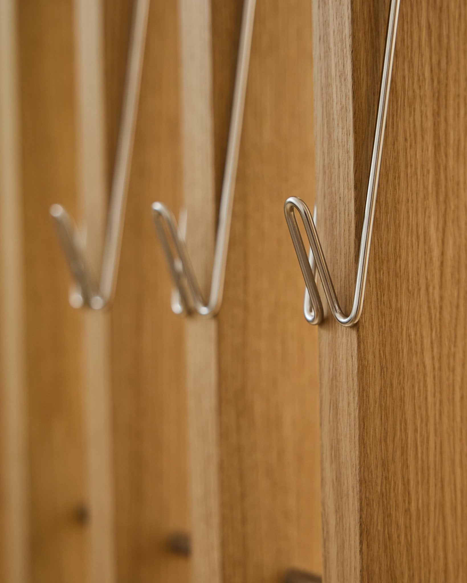 Close-up van drie Alva | Wire Hook / BM1, roestvrij Steel, lang, van WoodUpp, in een rij gemonteerd op Akupanel akoestische houten panelen en met zachte schaduwen.