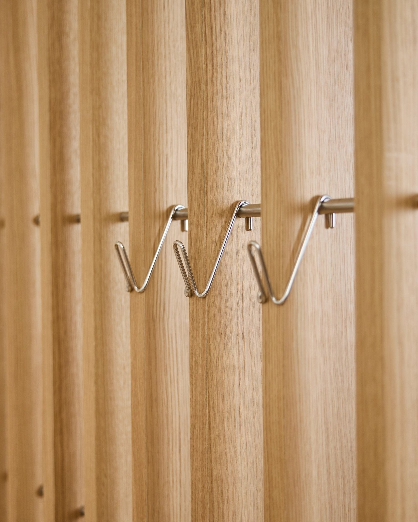 Drie korte roestvrijstalen steel WoodUpp Alva Wire Hook / BM1 accessoires zijn gelijkmatig naast elkaar gemonteerd op een vertical akoestisch houten lattenpaneel.