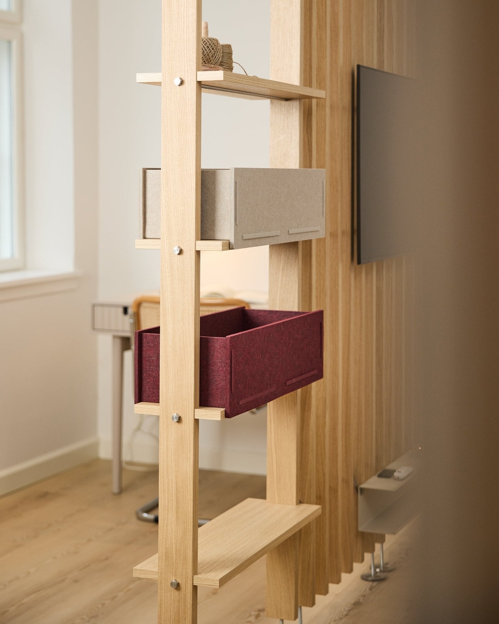 Op een WoodUpp-plank staan een beige opbergbox en een ox red Vigg Felt Box / BM2 in een lichte, minimalistische Scandinavische ruimte met akoestische houtdetails.