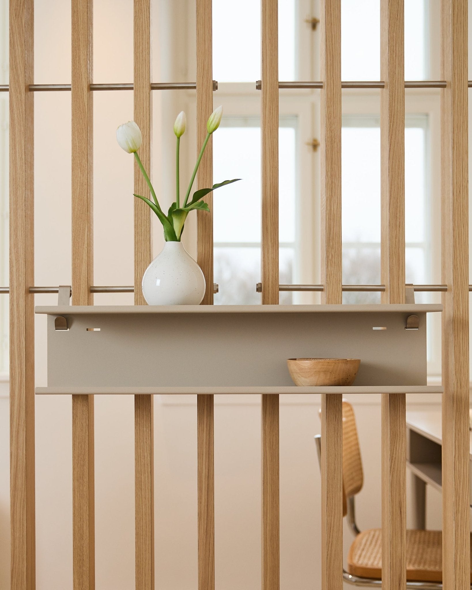 Double Metal Shelf / BM1 van WoodUpp in beige (63,5 cm), gemonteerd op een latten roomdivider, gestyled met een vaas en een houten schaal.