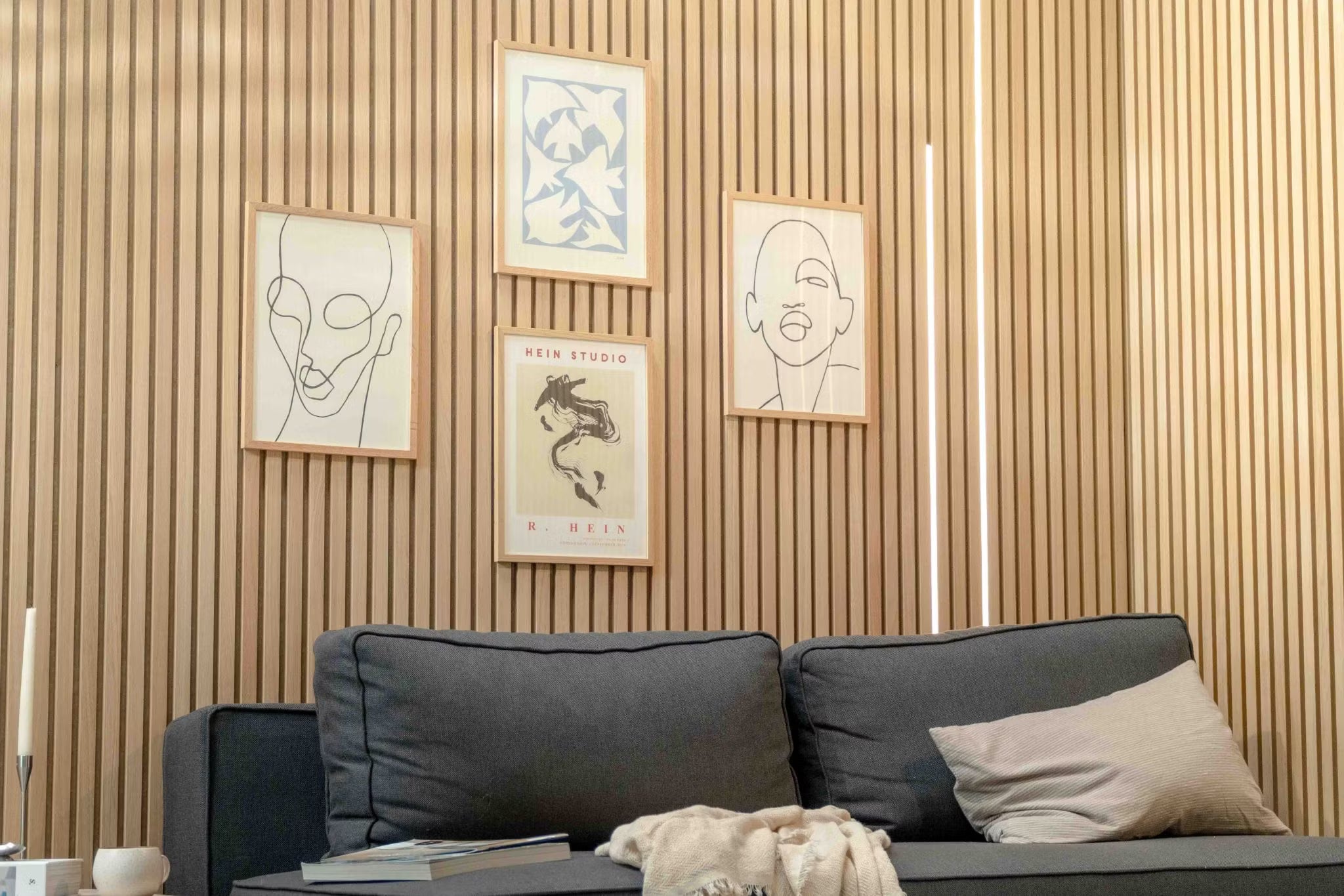 Moderne woonkamer met een donkere bank met een beige kussen, geaccentueerd door een Scandinavische Akupanel akoestische houten lattenwand en minimalistische Scandinavische kunst erboven.